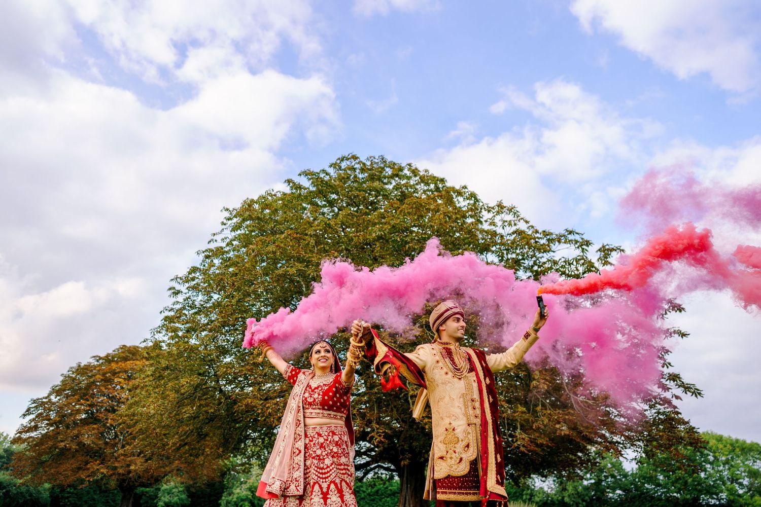 Wedding celebration under blue skies with pink smoke effects creating a dramatic atmosphere.