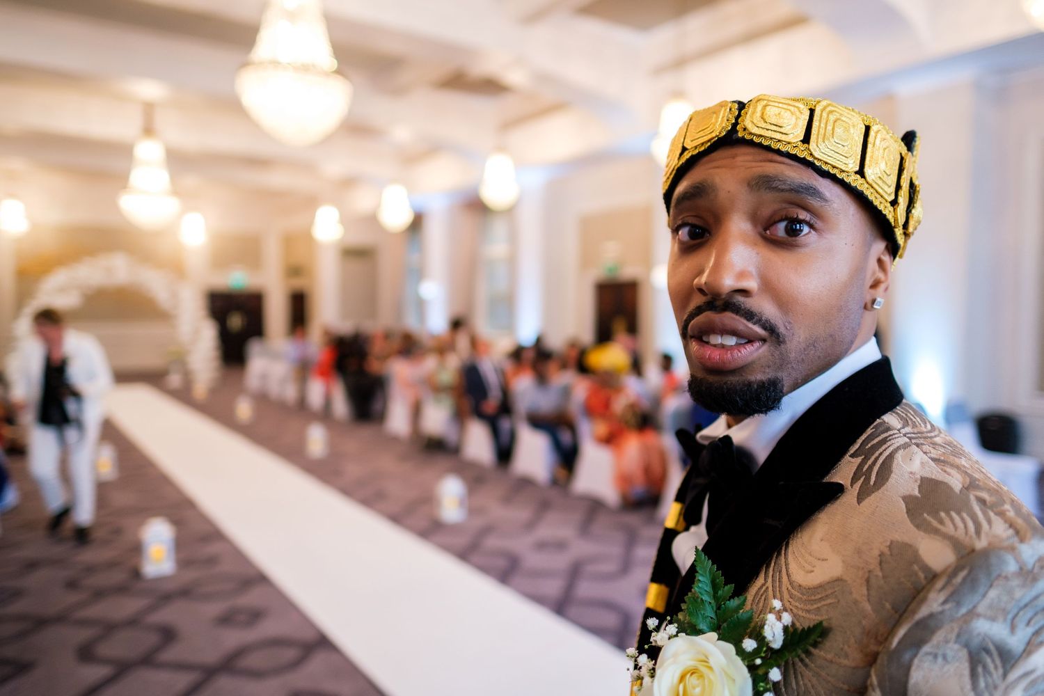 Person wearing a gold crown and brown jacket at an elegant indoor event.