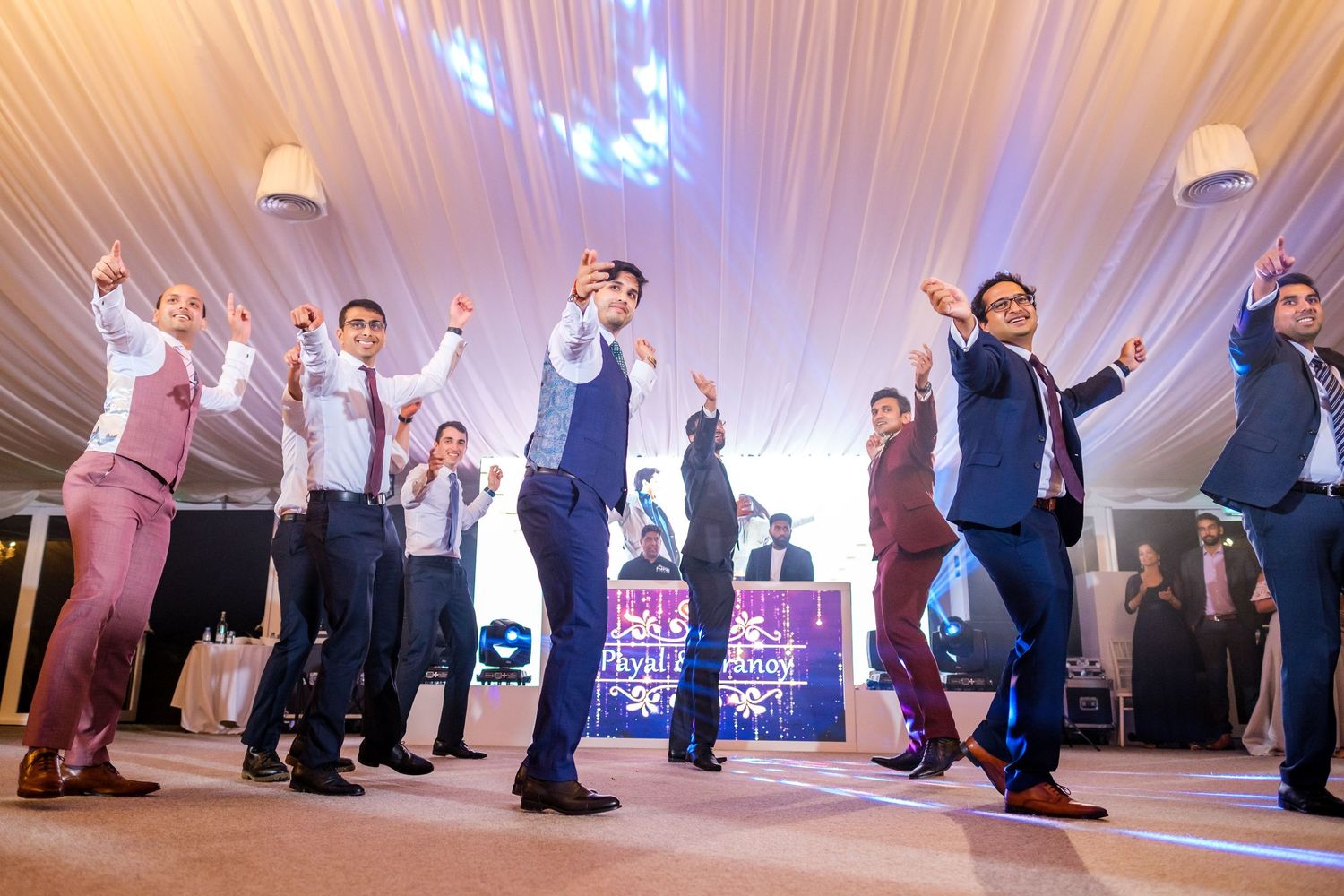 Wedding reception dance floor with guests celebrating under white draped ceiling and blue lighting.