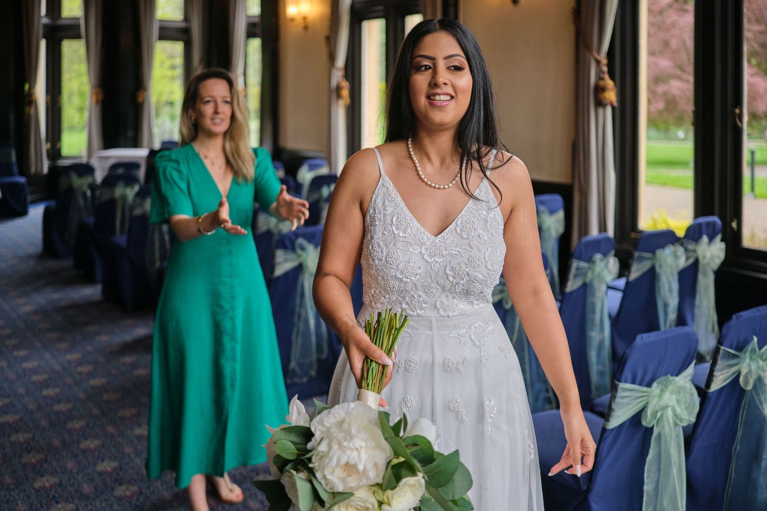 A person in a white dress holds a bouquet while standing in an elegant venue with blue chair decor.