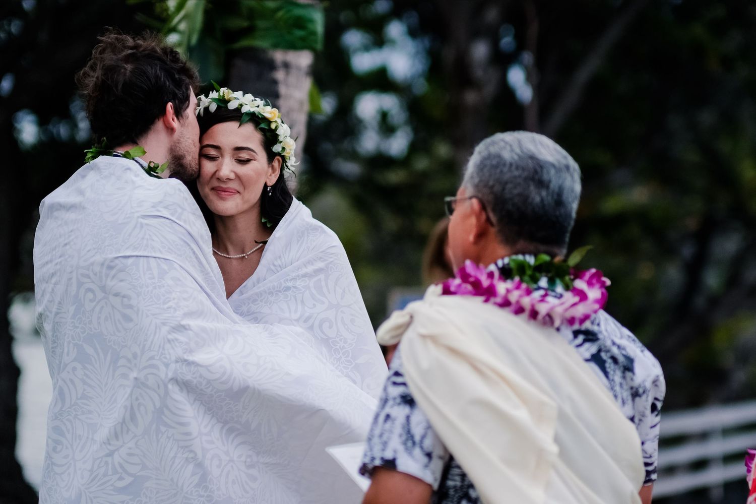 Wedding party relaxing on grass wearing floral leis and casual attire during outdoor celebration.