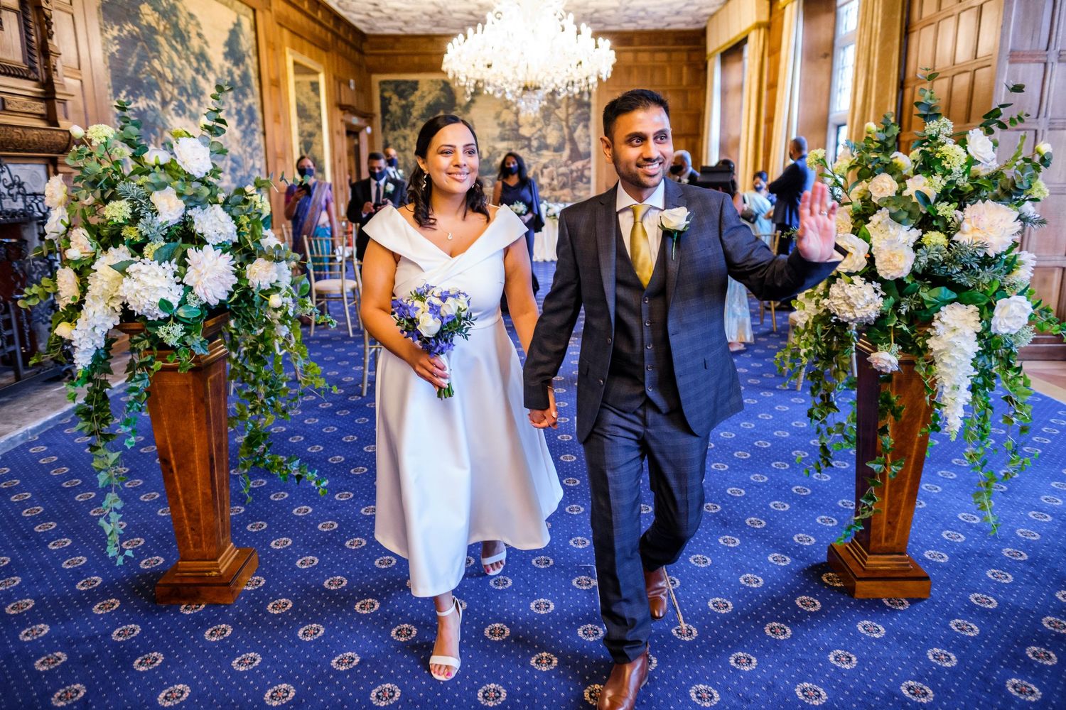 Elegant wedding ceremony in a grand ballroom with crystal chandeliers and ornate blue carpeting.