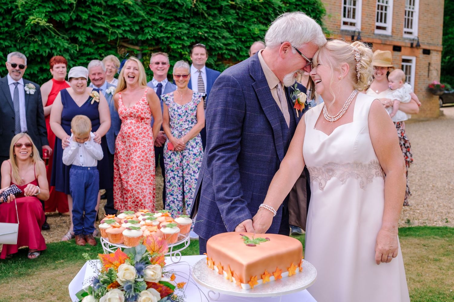 Wedding guests gather outdoors on a sunny day to celebrate with cake and refreshments.