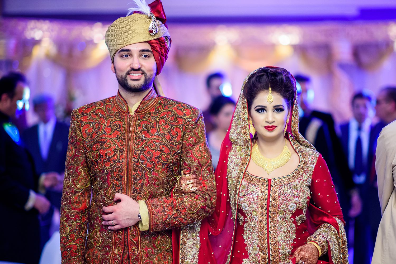 Wedding ceremony in a purple-lit venue featuring traditional South Asian formal attire.