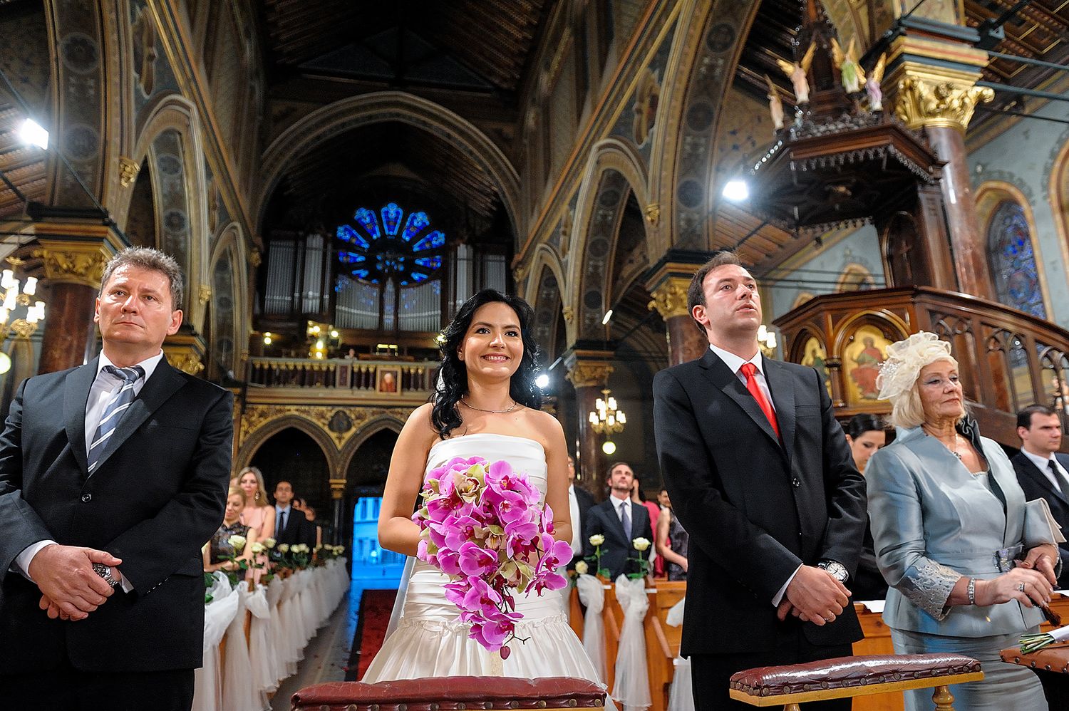 Wedding ceremony inside an ornate church with decorative arches and stained glass windows.