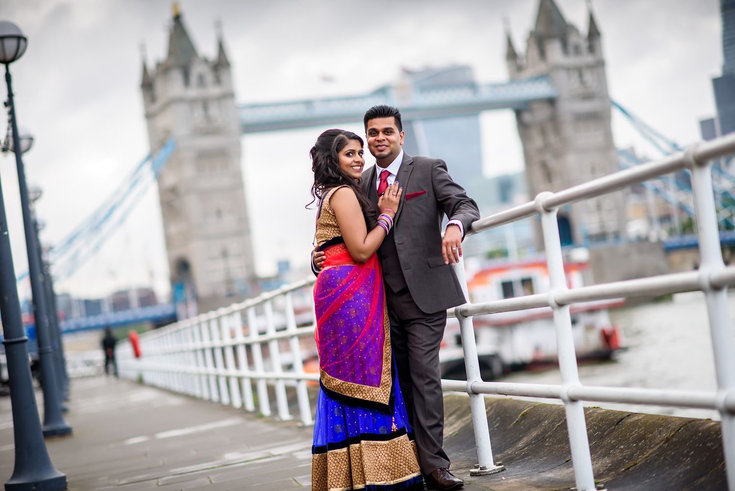 A couple embraces on a walkway with Tower Bridge of London in the background.