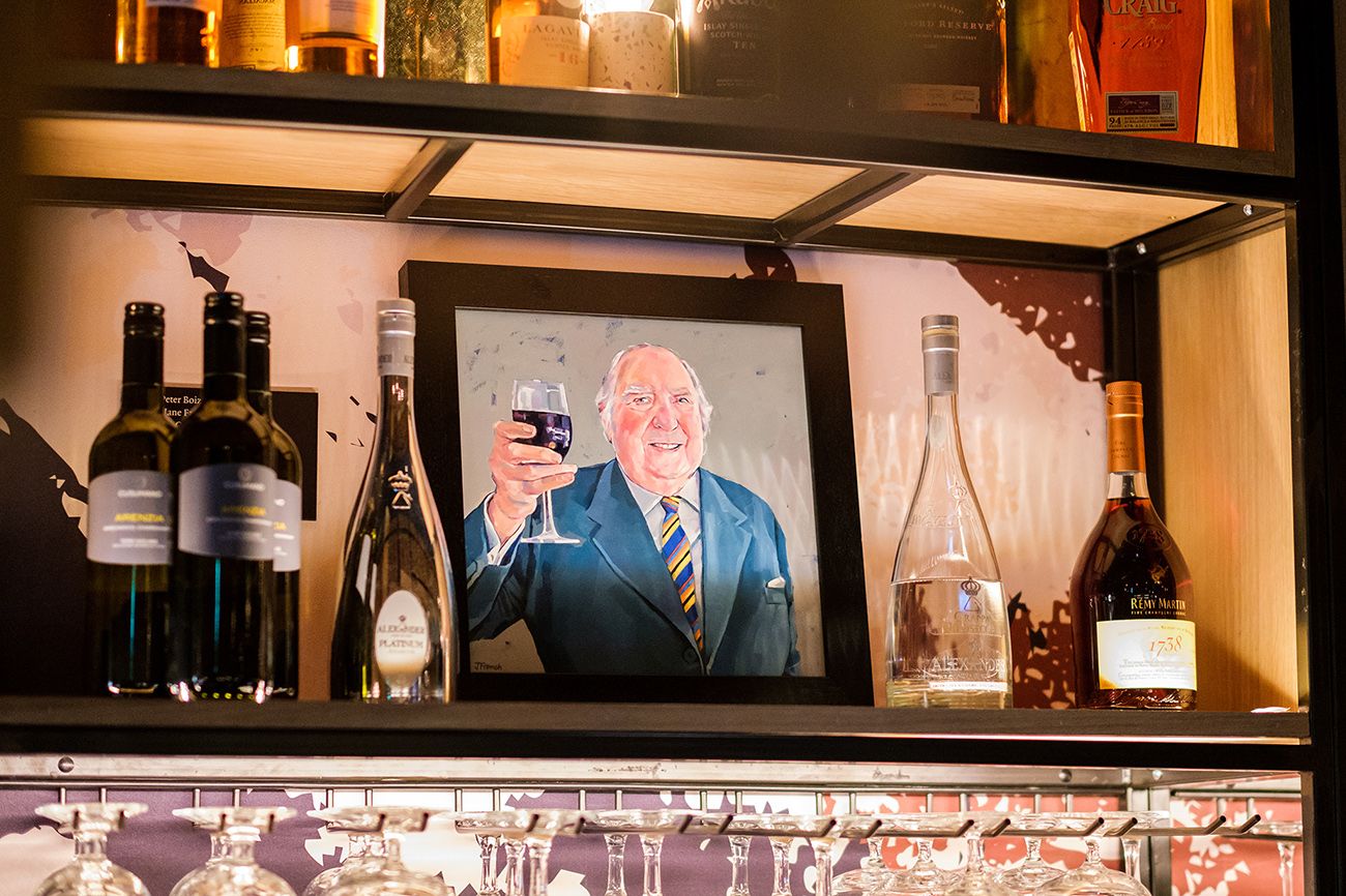 Bar interior with illuminated shelves displaying bottles and screens showing entertainment content.