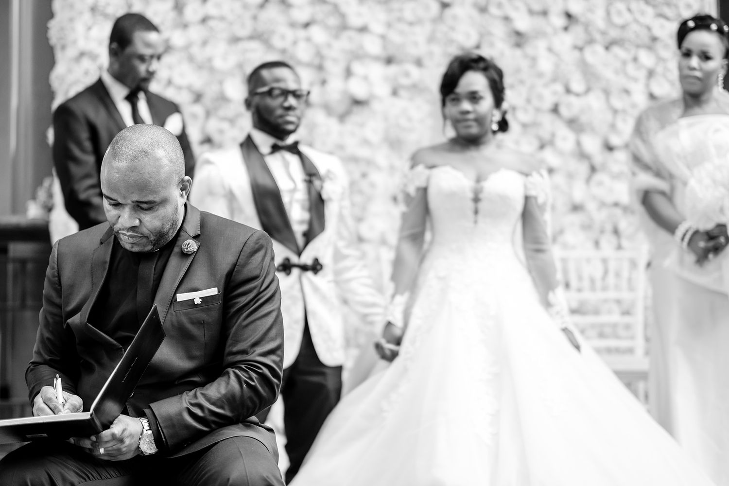 Formal wedding ceremony in front of elegant white floral backdrop.