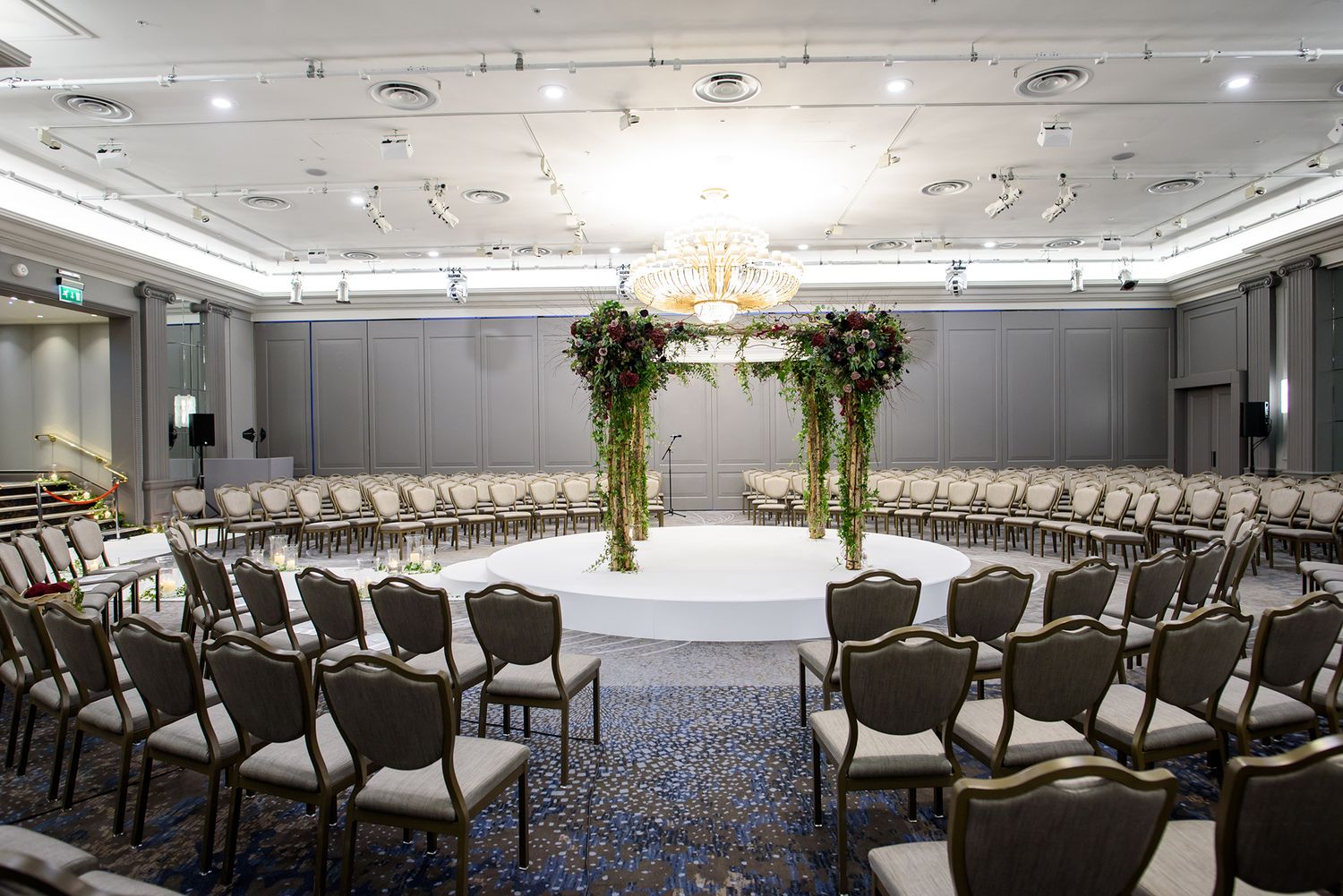 Modern wedding ceremony setup with chairs arranged in circles around a floral arch centerpiece.