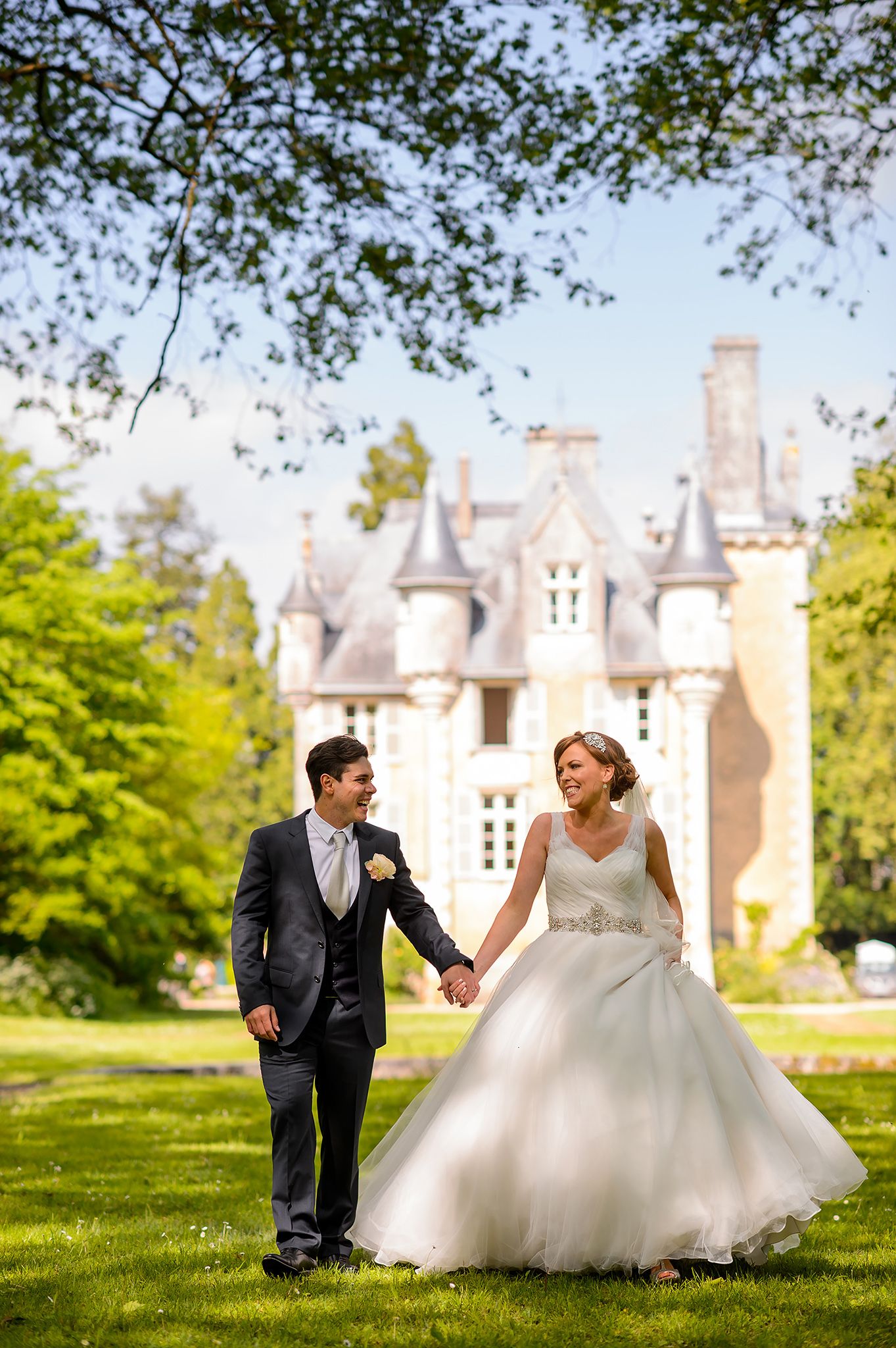 Wedding couple sits on grass with elegant castle venue in background.