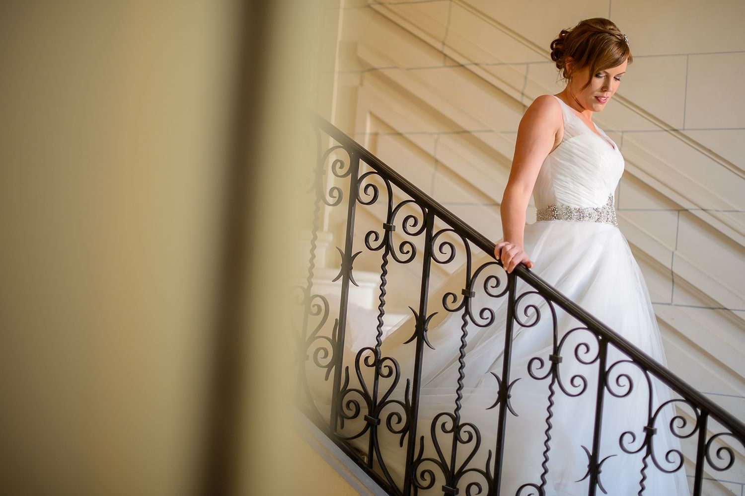Aerial view of bride descending ornate spiral staircase in flowing white wedding dress.