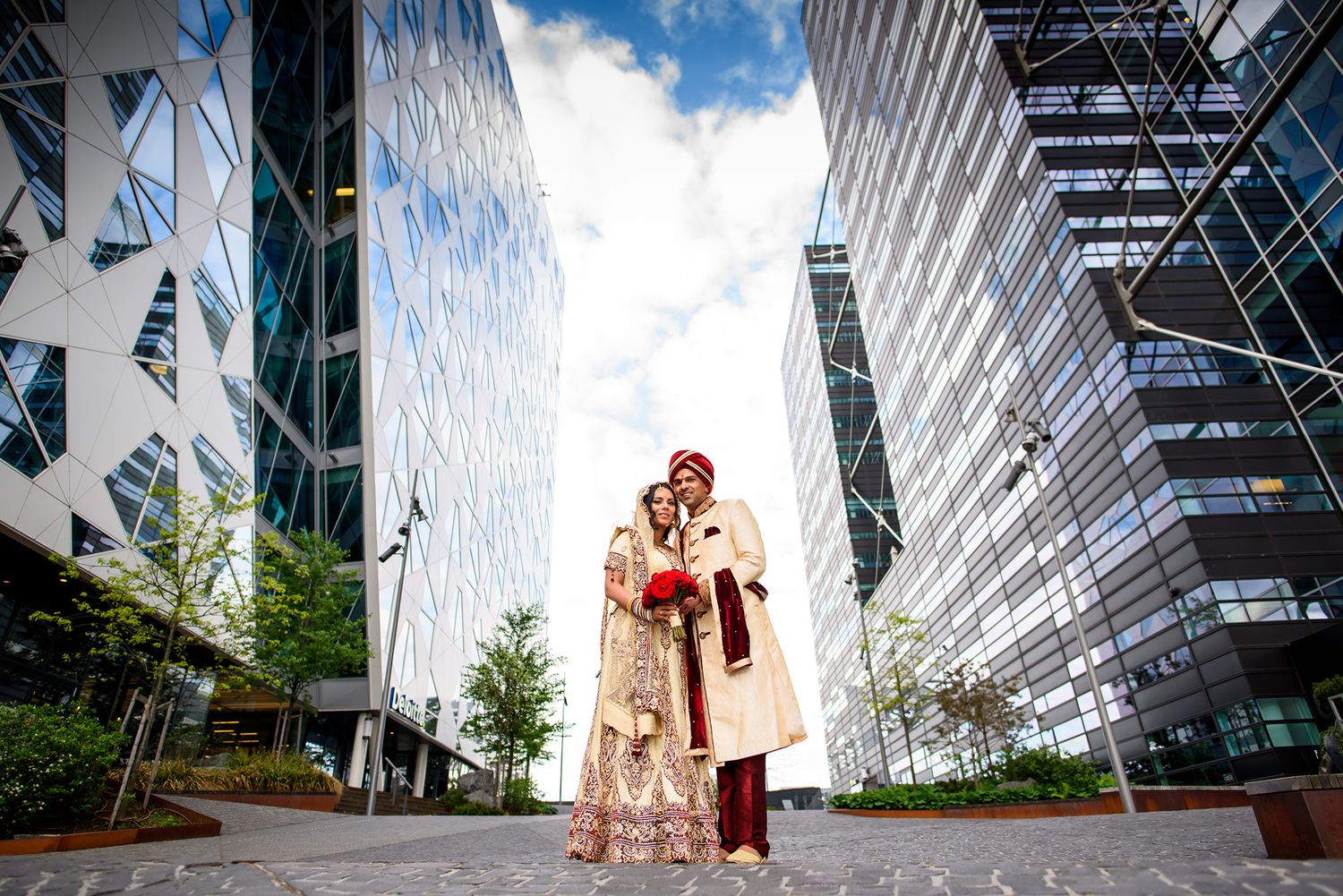 Modern glass buildings provide dramatic backdrop for wedding photos in urban setting.
