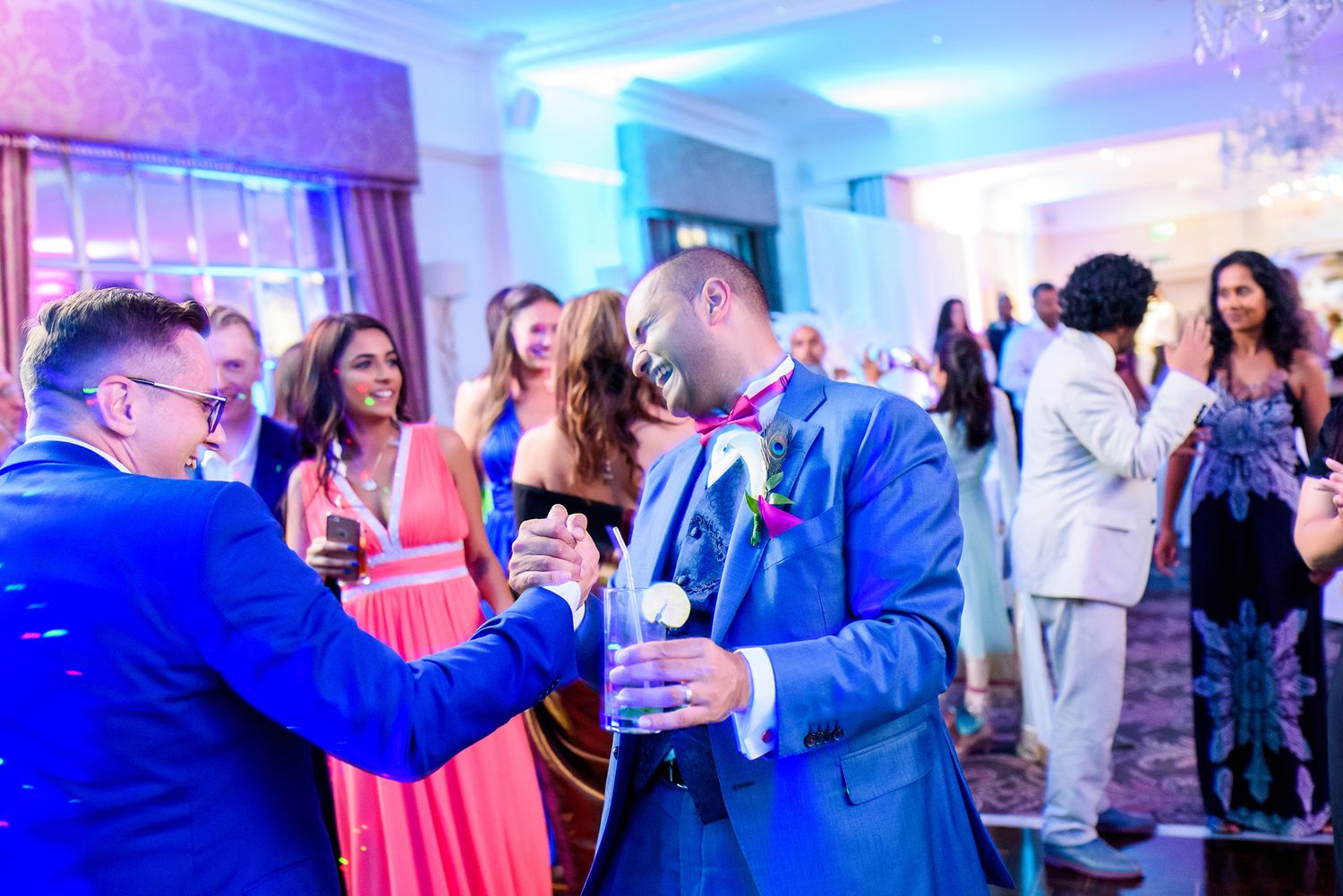 Wedding reception venue illuminated with vibrant blue and pink lighting during evening celebration.