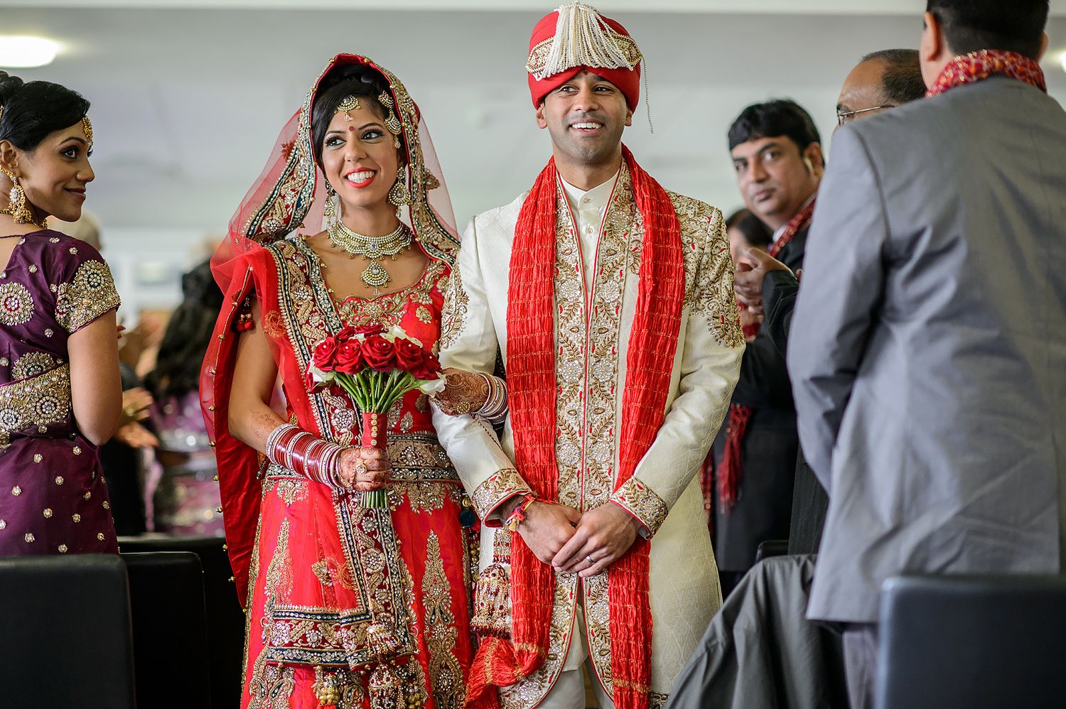 Wedding couple in traditional red and gold Indian wedding attire during ceremony proceedings.