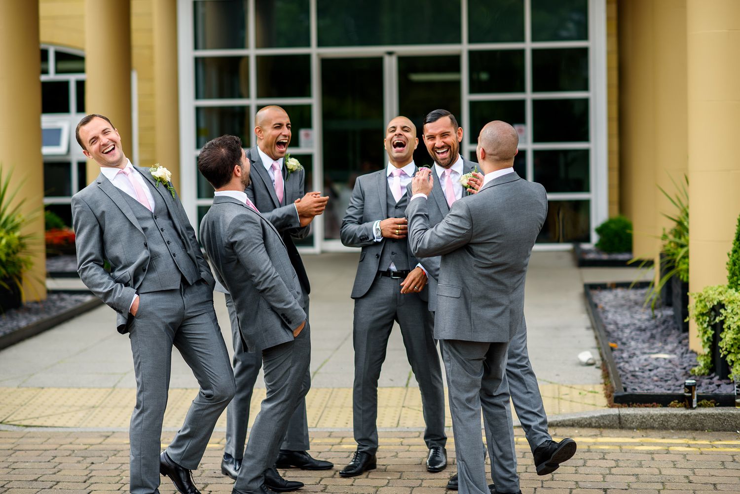Groomsmen in grey suits perform a fun jumping pose outside a building.