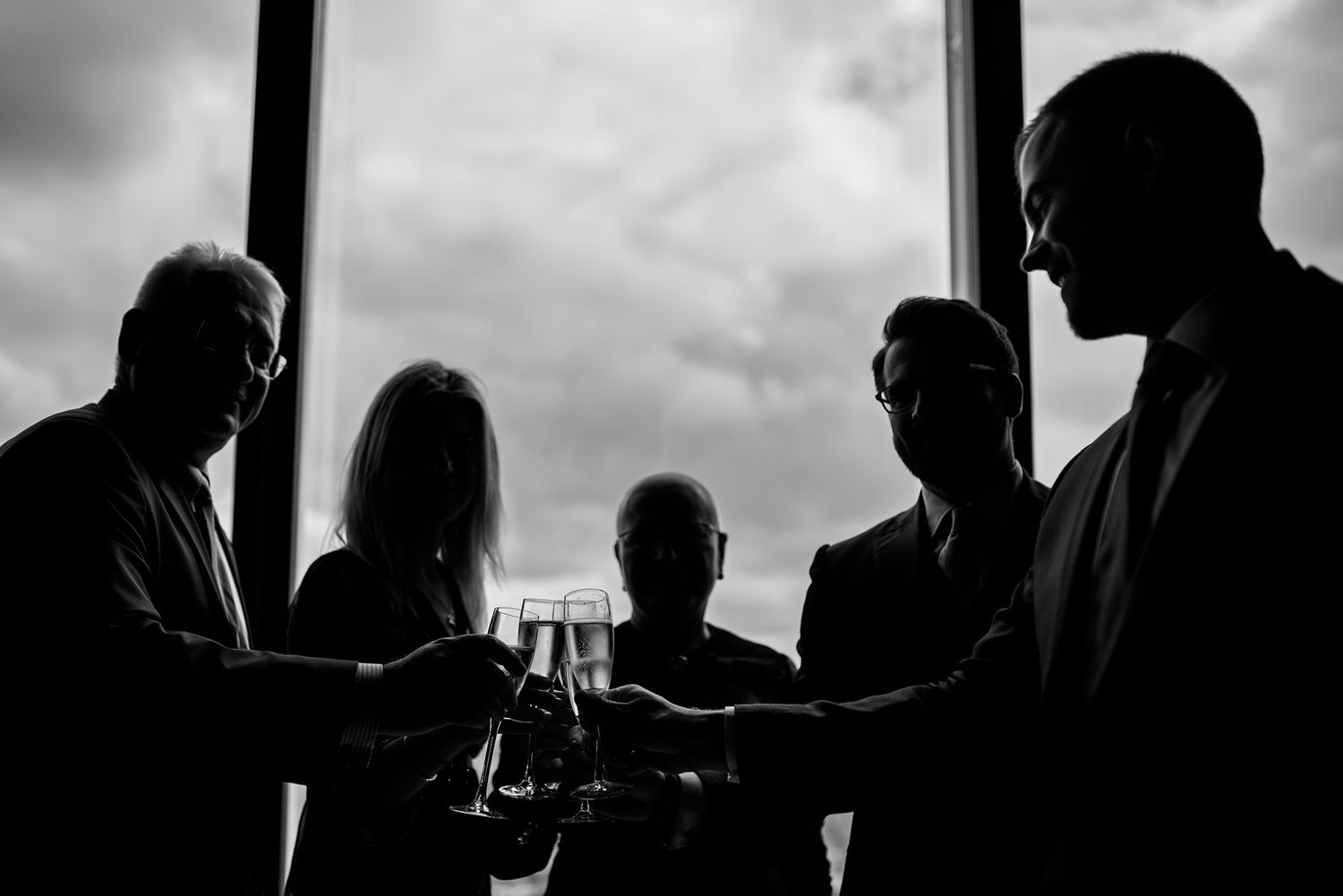 Dramatic silhouette of dining guests against cloudy sky through large windows.