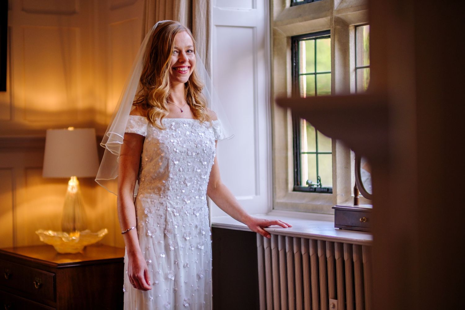 Elegant white lace wedding dress photographed in natural window light inside a historic building.