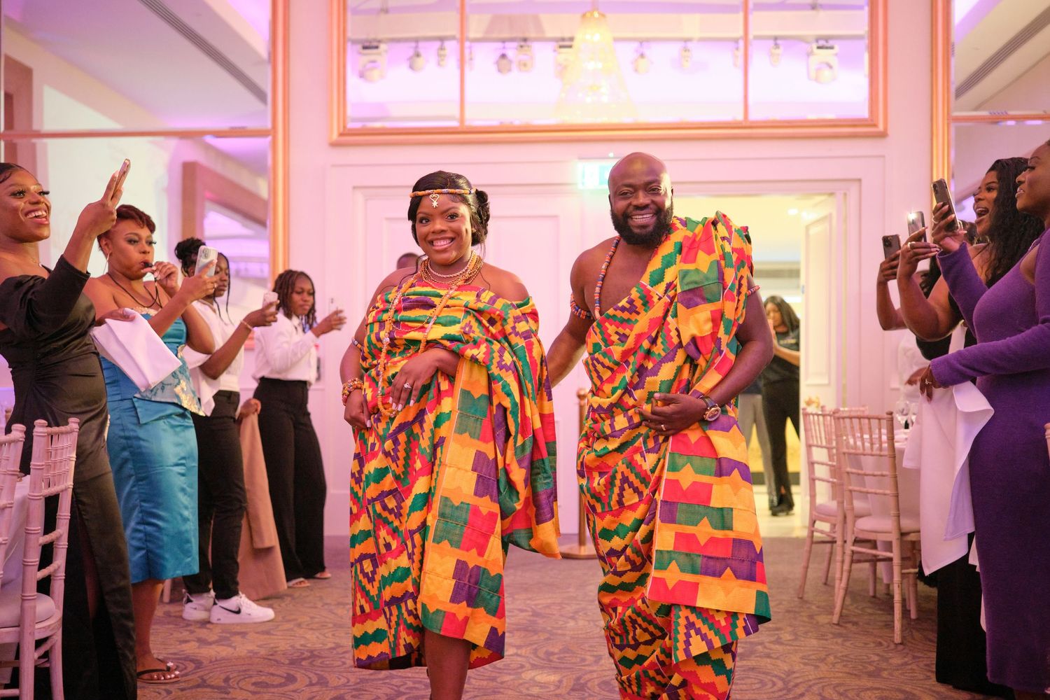 Wedding celebration with guests dancing and mingling in an elegant reception hall decorated with pink lighting.
