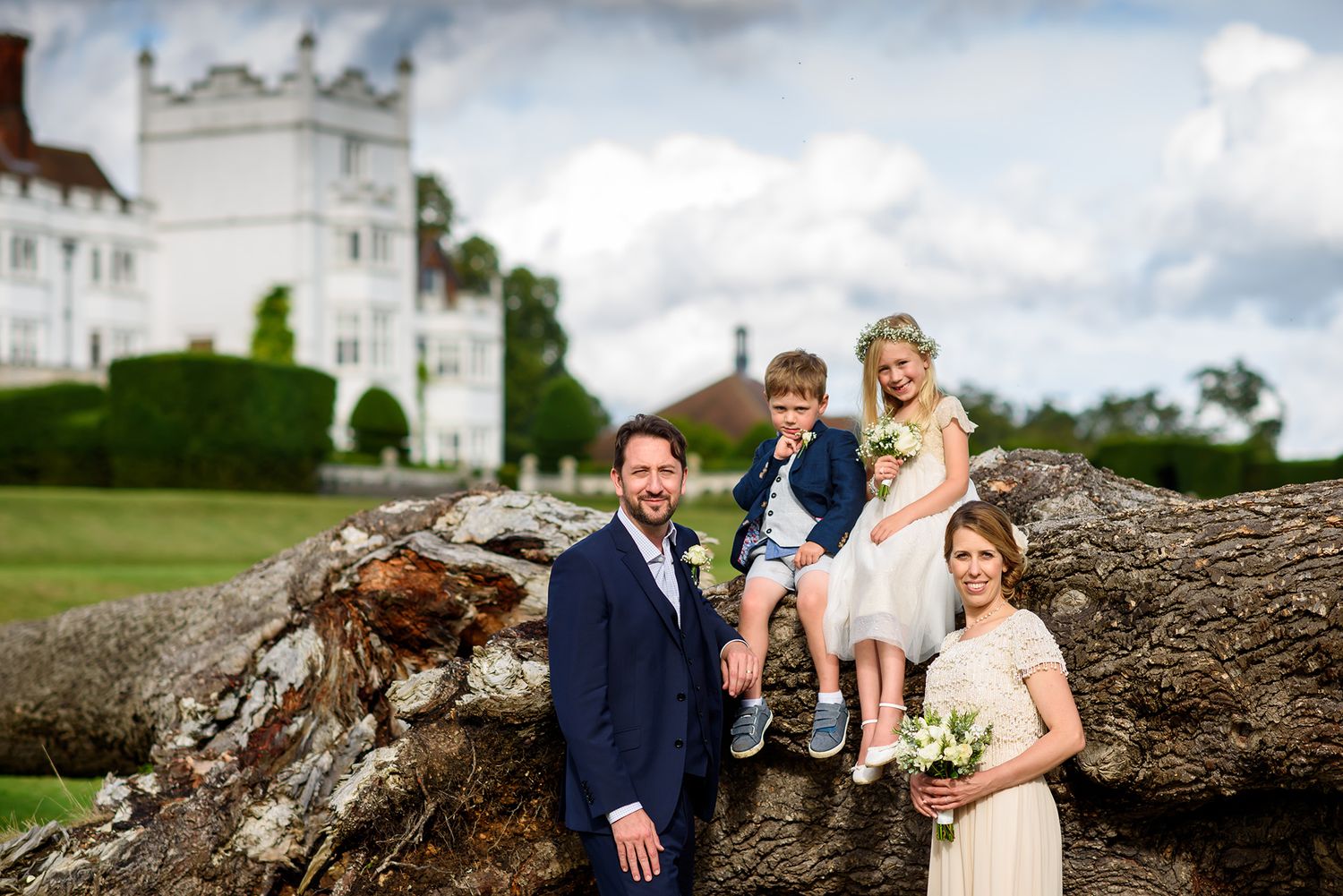 Wedding party poses near white church building on grassy hillside.