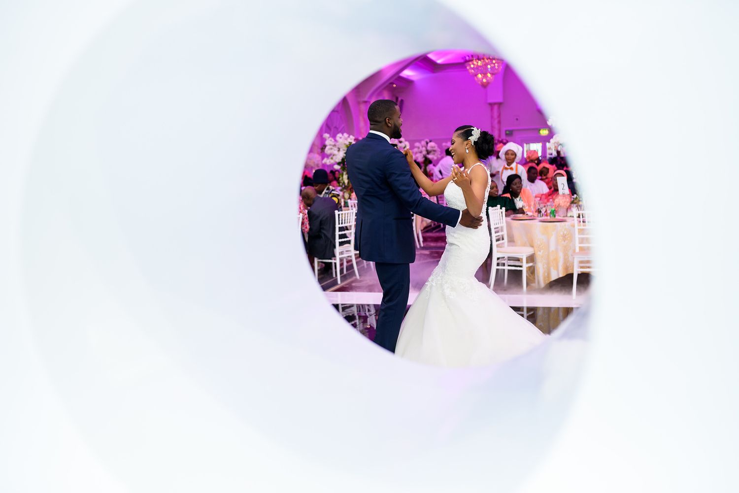 Artistic wedding photo through a circular window frame showing the couple dancing.
