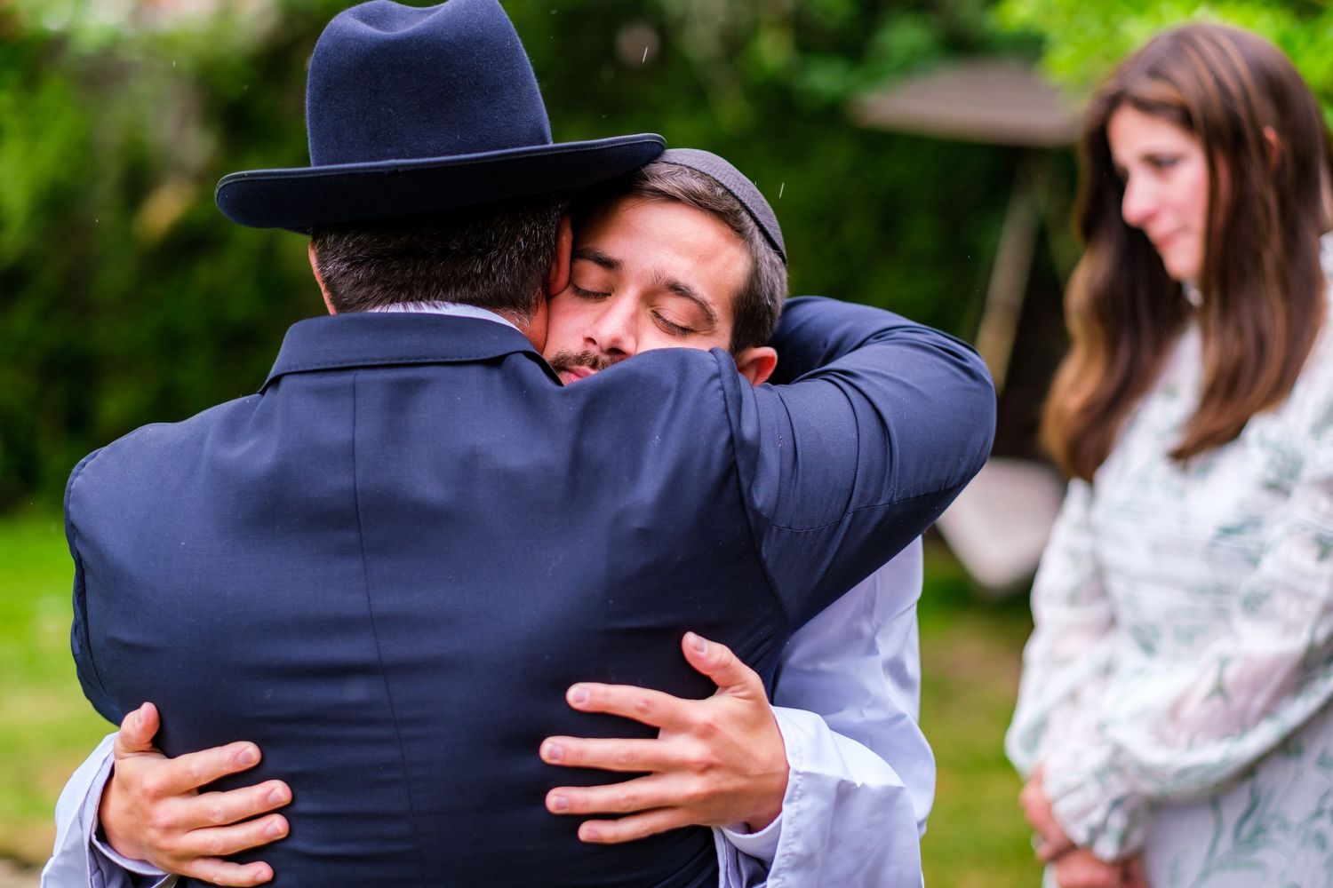 A group of people sharing emotional embraces outdoors in a garden setting.