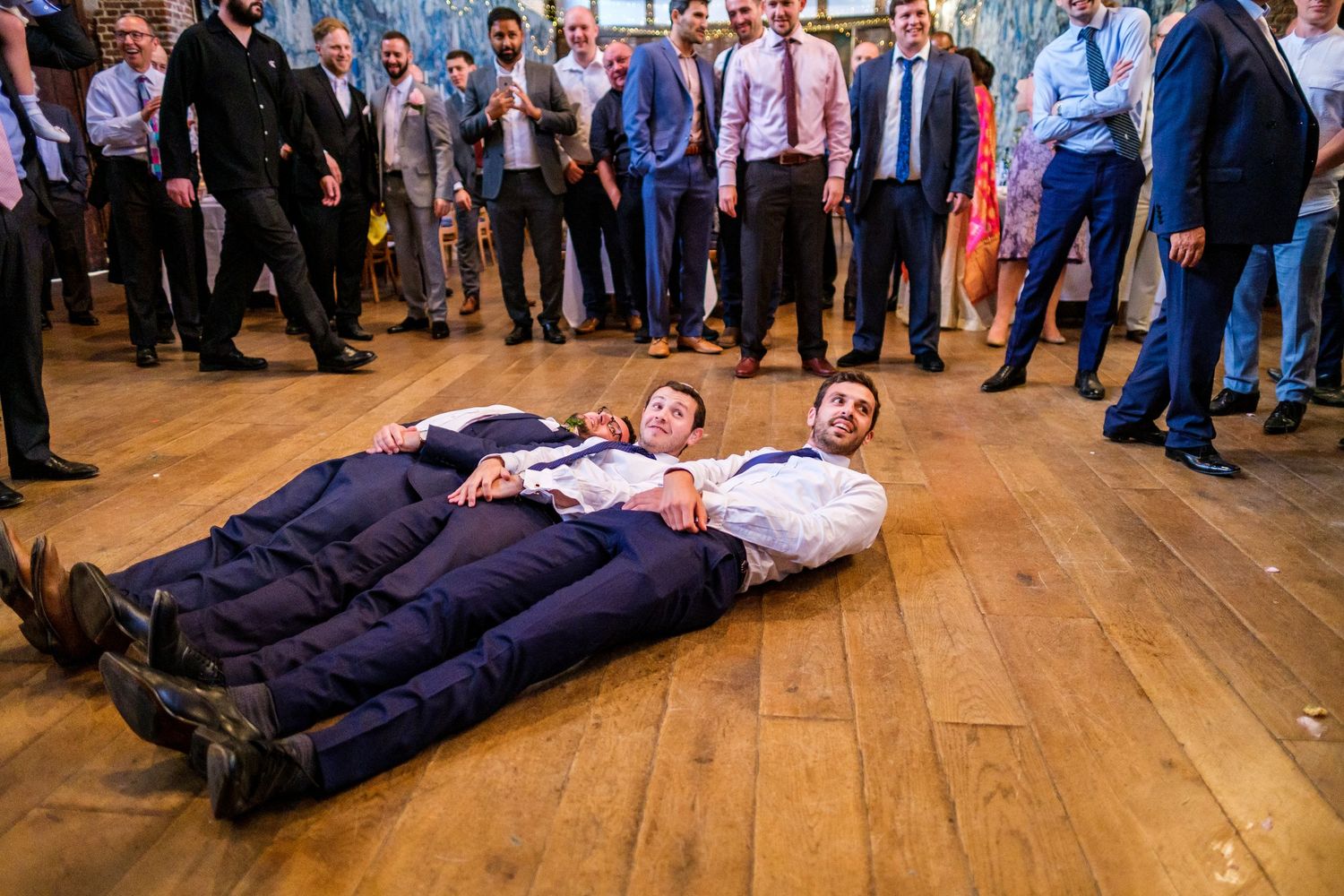 Wedding party lying on wooden floor in a fun group photo formation.
