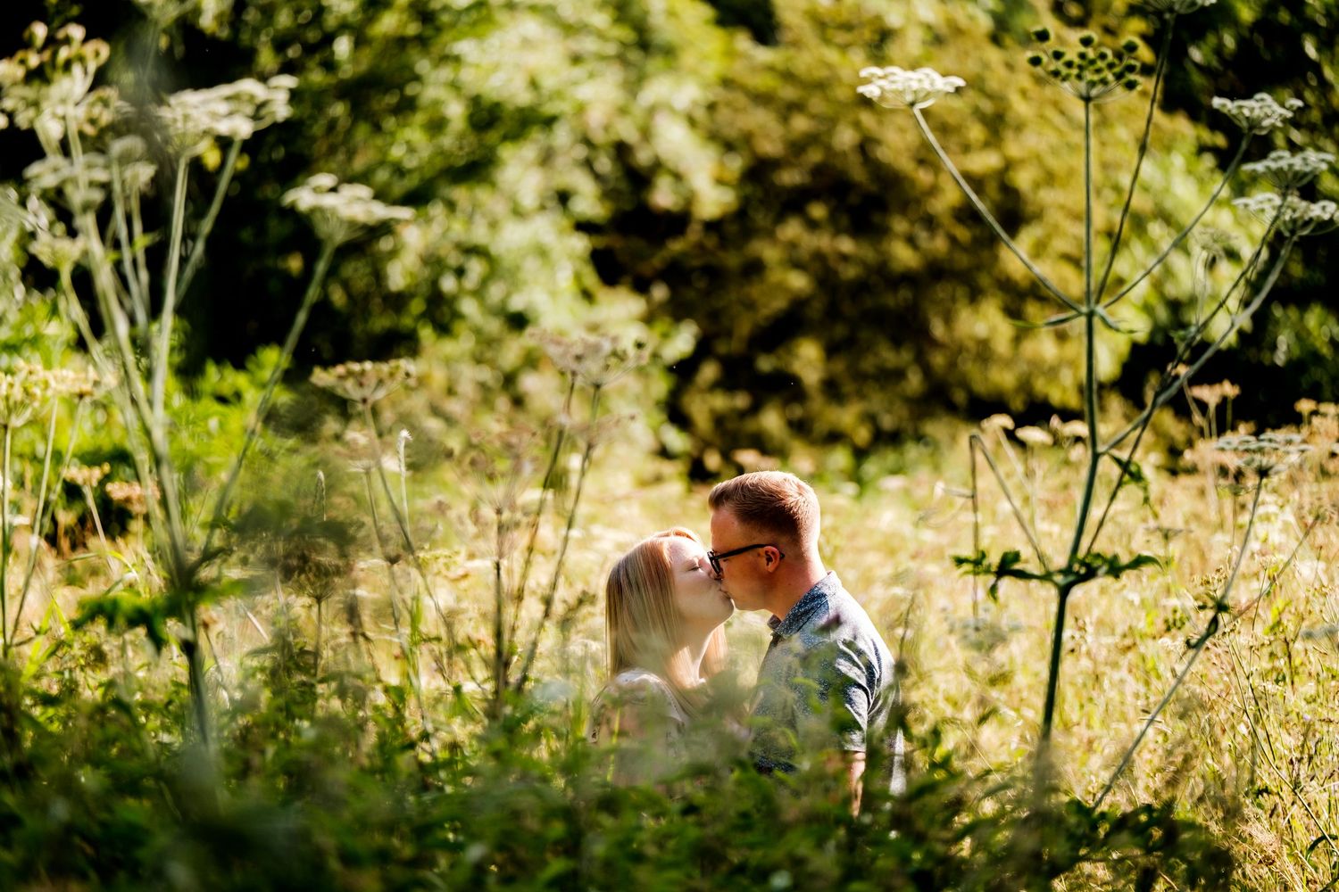 A romantic moment captured in tall golden grass with sunlit bokeh.