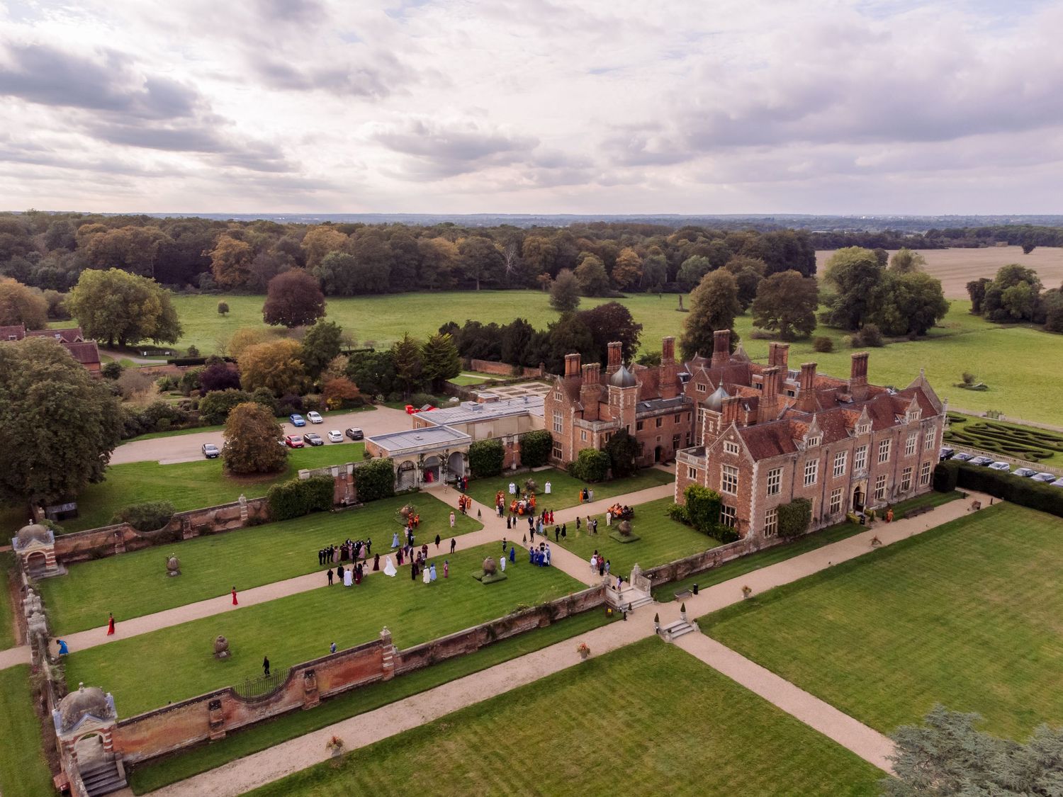Aerial view of a grand estate with manicured lawns and historic architecture on a cloudy autumn day.