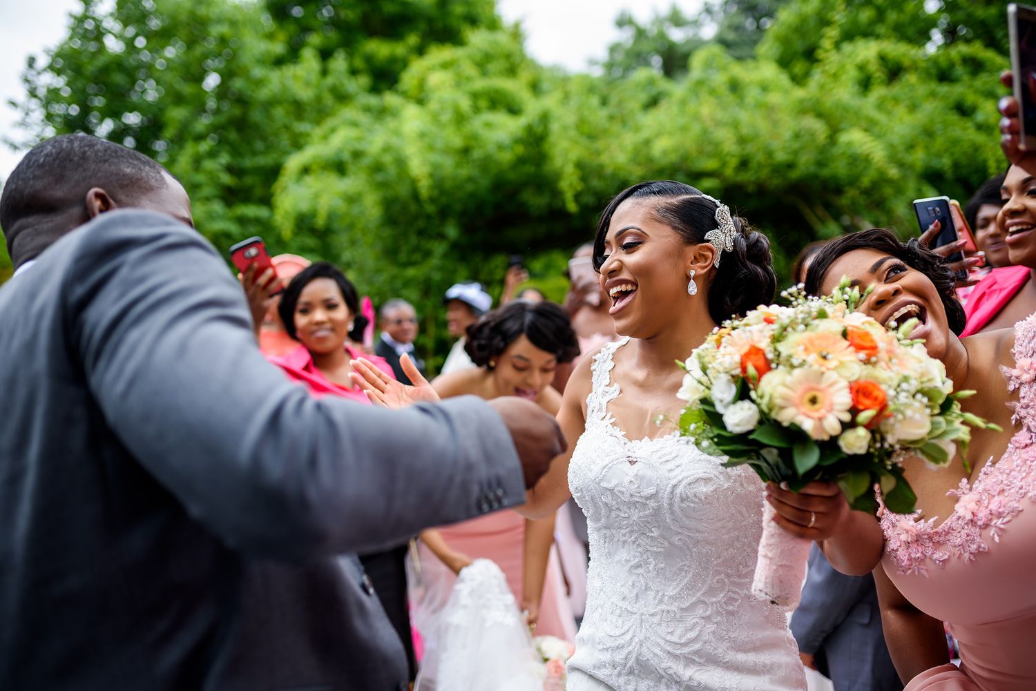 Bride in lace dress celebrates with wedding party members in a verdant garden setting.
