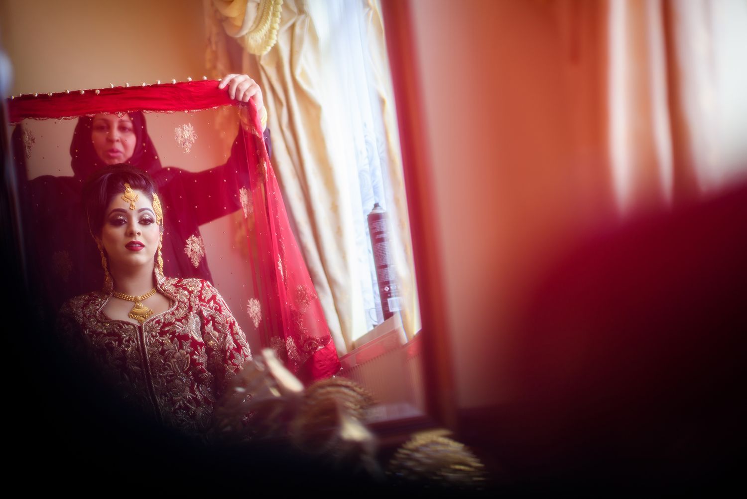 Soft red-tinted bridal preparation scene through a window reflection.