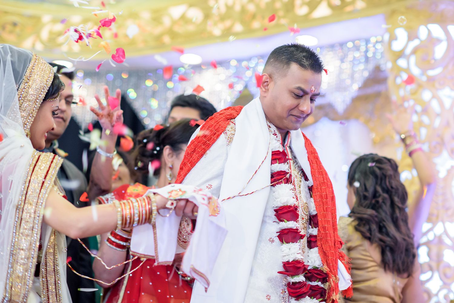 Wedding ceremony moments with red and white floral decorations and confetti.