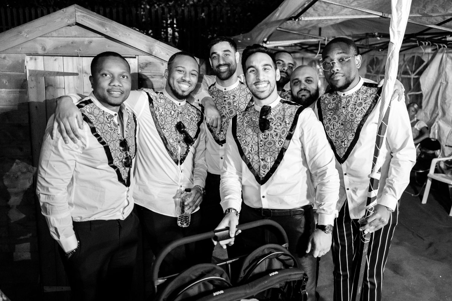 Groomsmen in matching vests pose together for a black and white group photo.