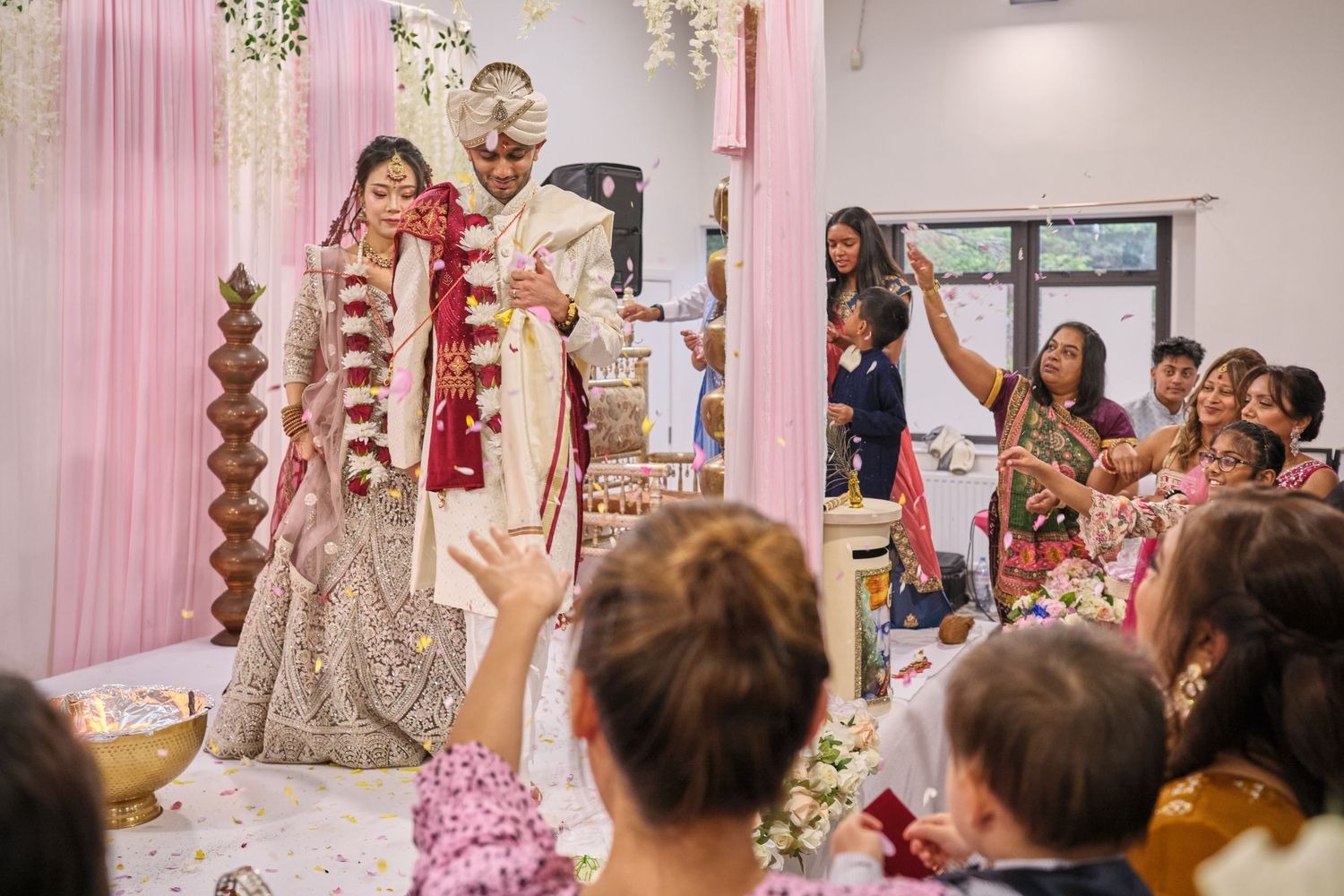 Wedding guests celebrating during a ceremony in a decorated indoor venue with pink accents.