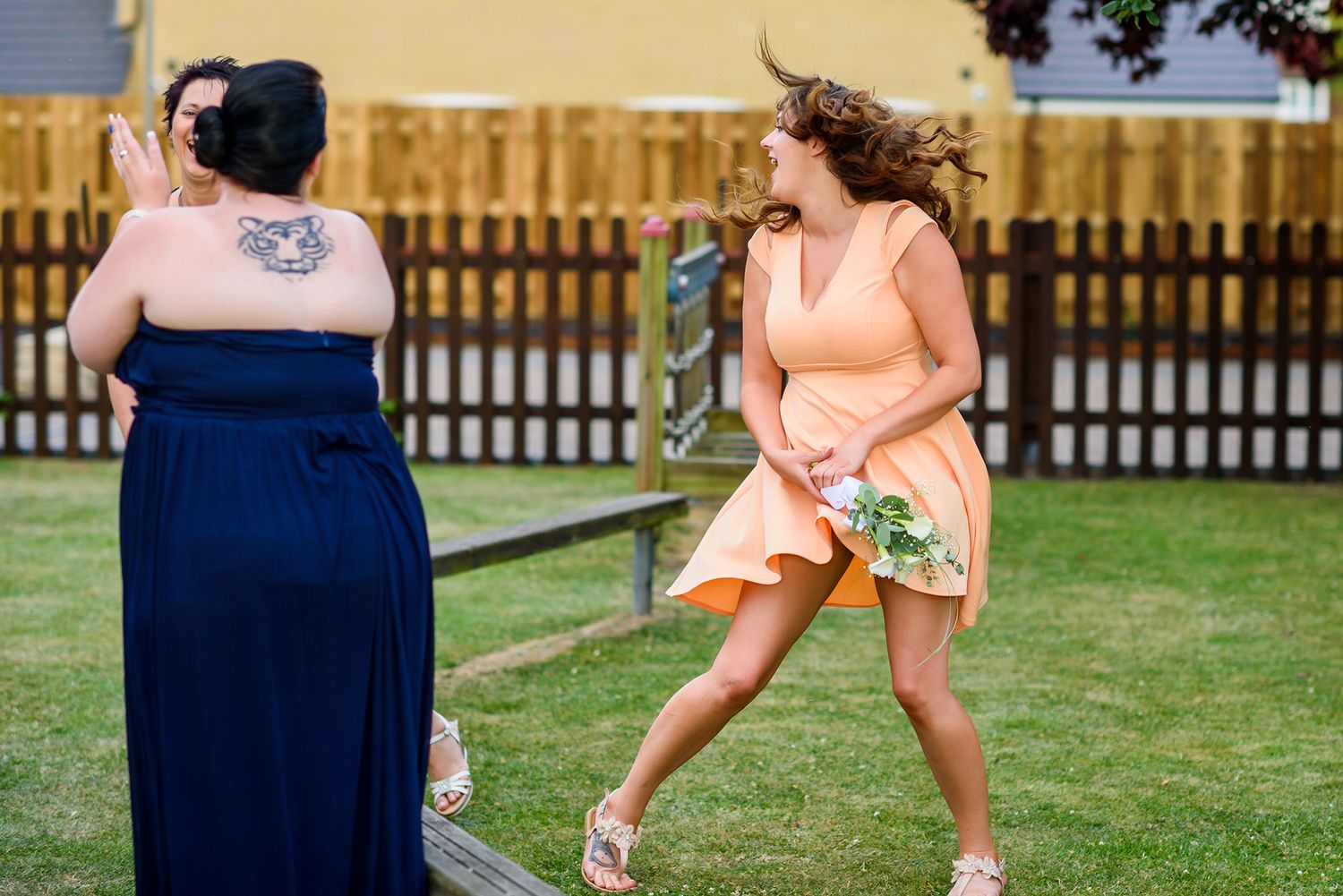 Wedding guests in navy dresses dance and celebrate outdoors on a grassy lawn during a reception.