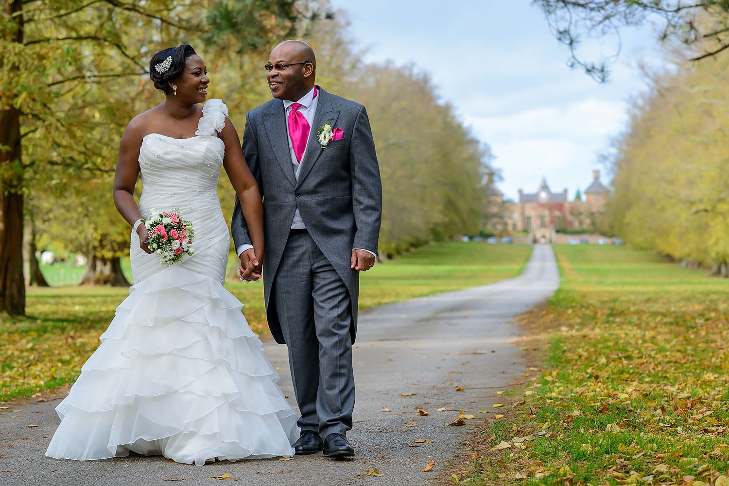 Wedding couple strolls along tree-lined path during autumn photoshoot.