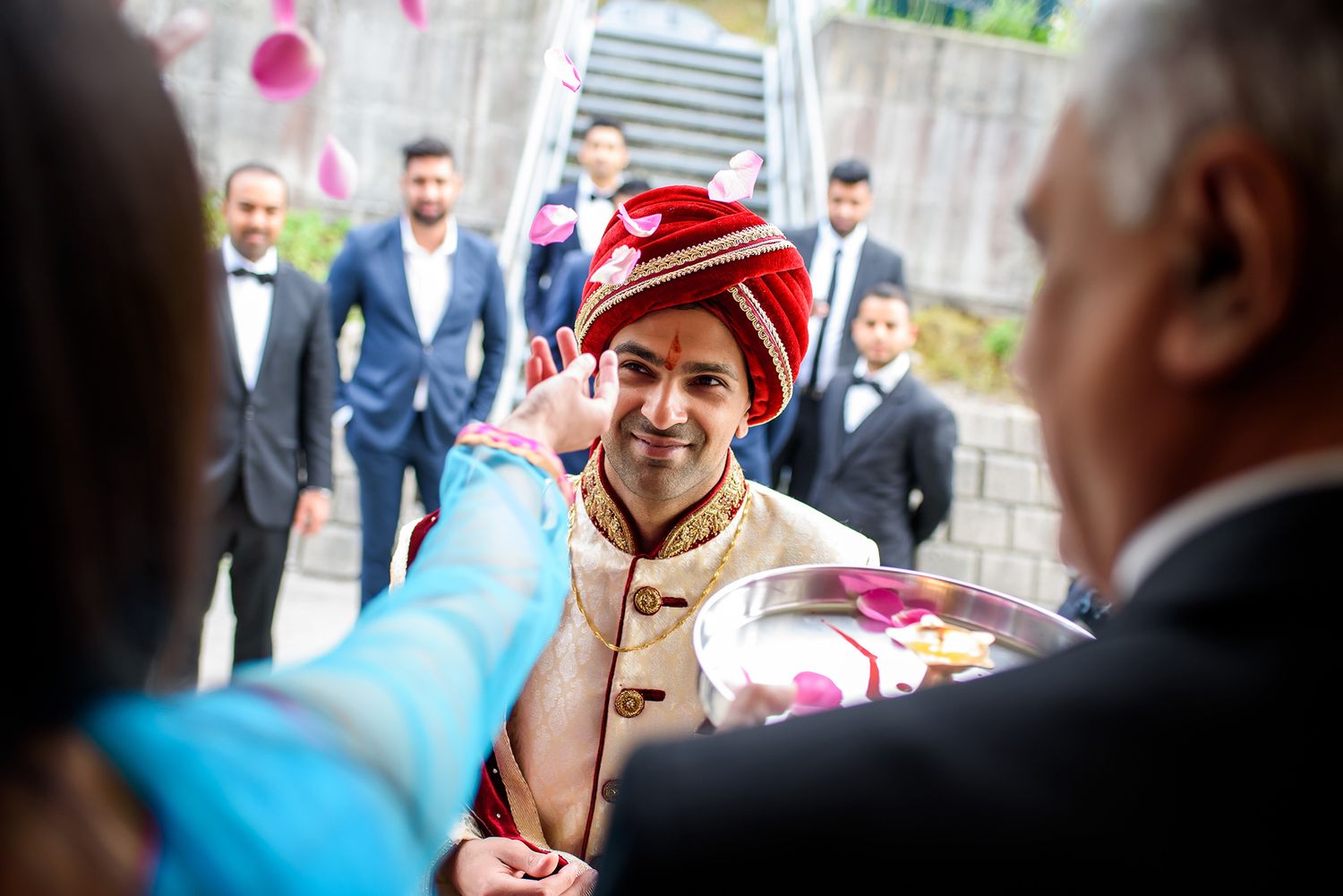 Groom in traditional Indian attire with red turban and beige sherwani smiling at wedding ceremony.