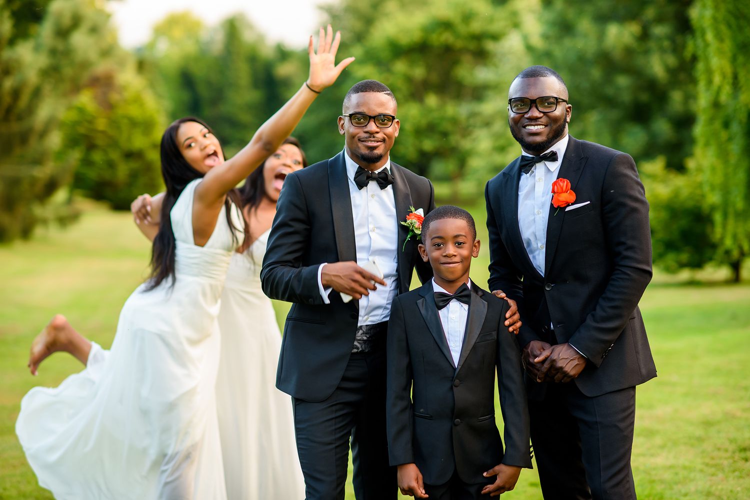 Groomsmen in black tuxedos celebrate joyfully outdoors during wedding festivities.