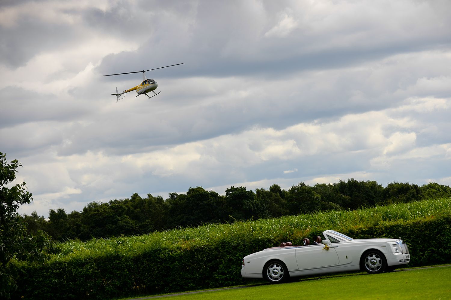 White luxury convertible car and helicopter against cloudy sky.
