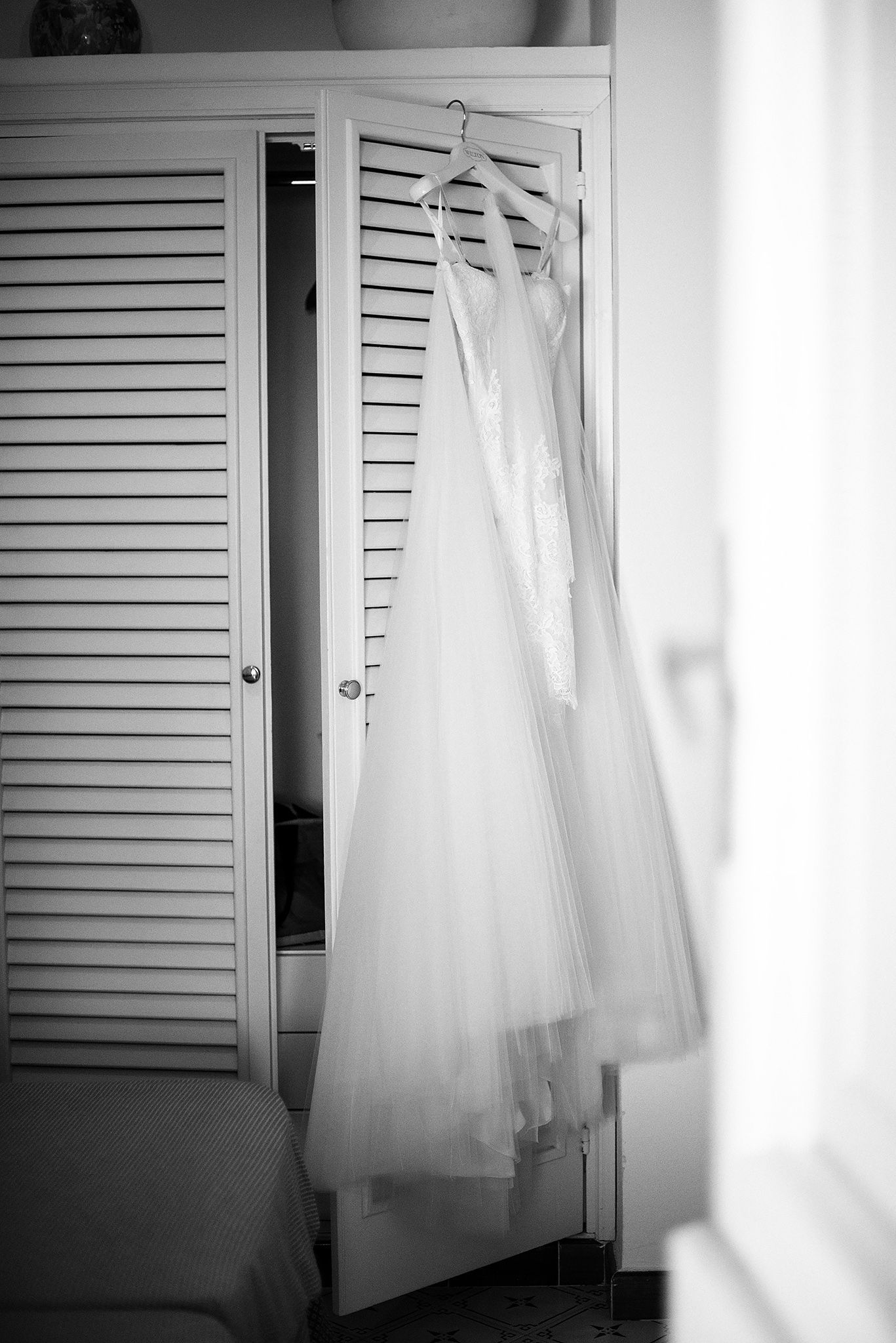 Minimalist black and white photo of wedding dresses against louvered doors.