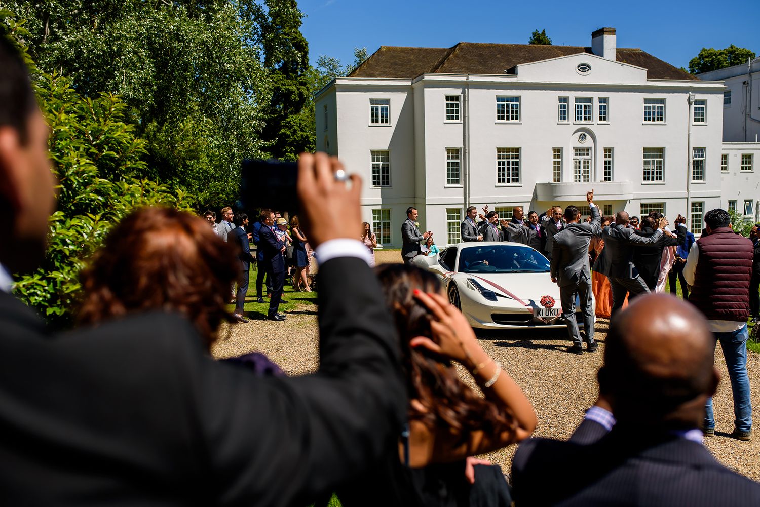 Panoramic view of a white manor house with wedding guests gathered outside.