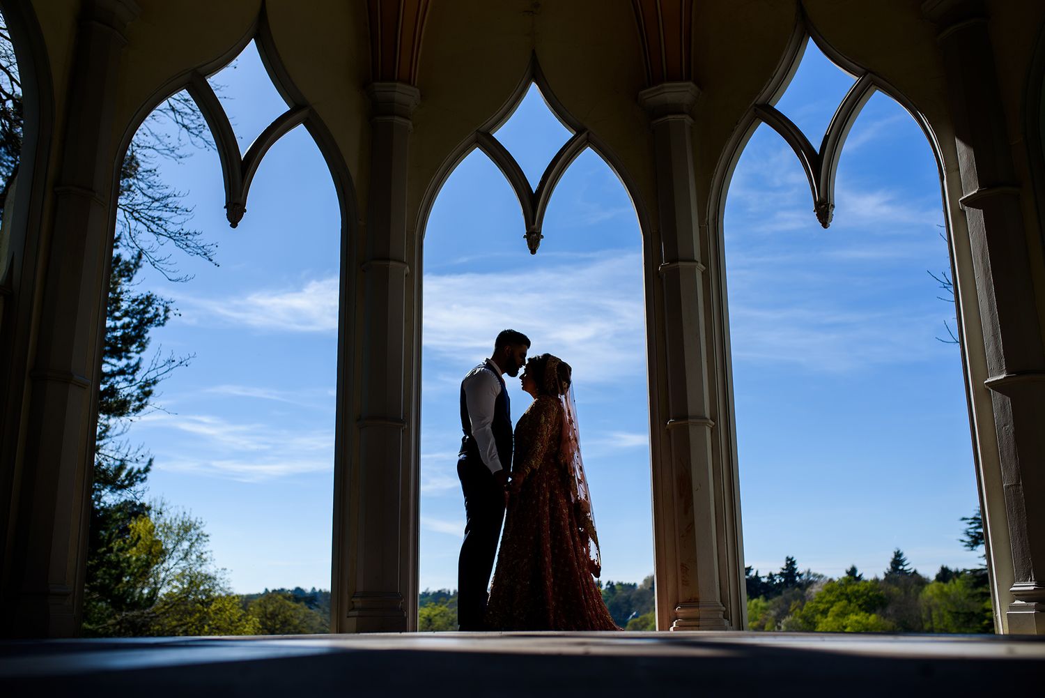 Elegant outdoor archway silhouettes against blue sky create romantic wedding ceremony backdrop.