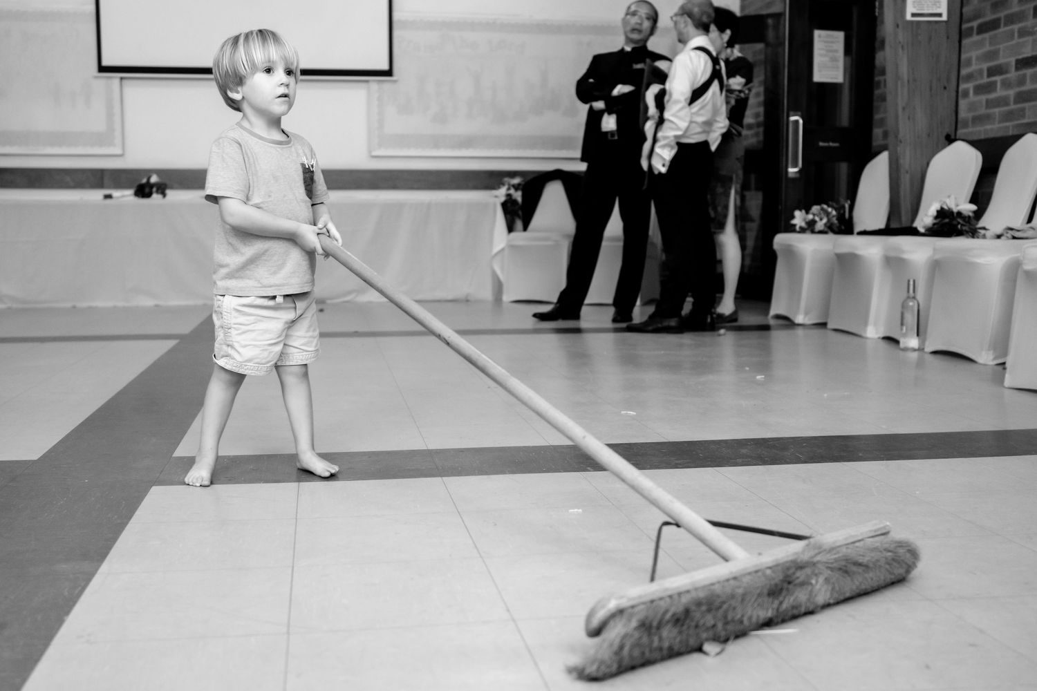 A person performs a curling sweep technique on an indoor ice rink during a match.