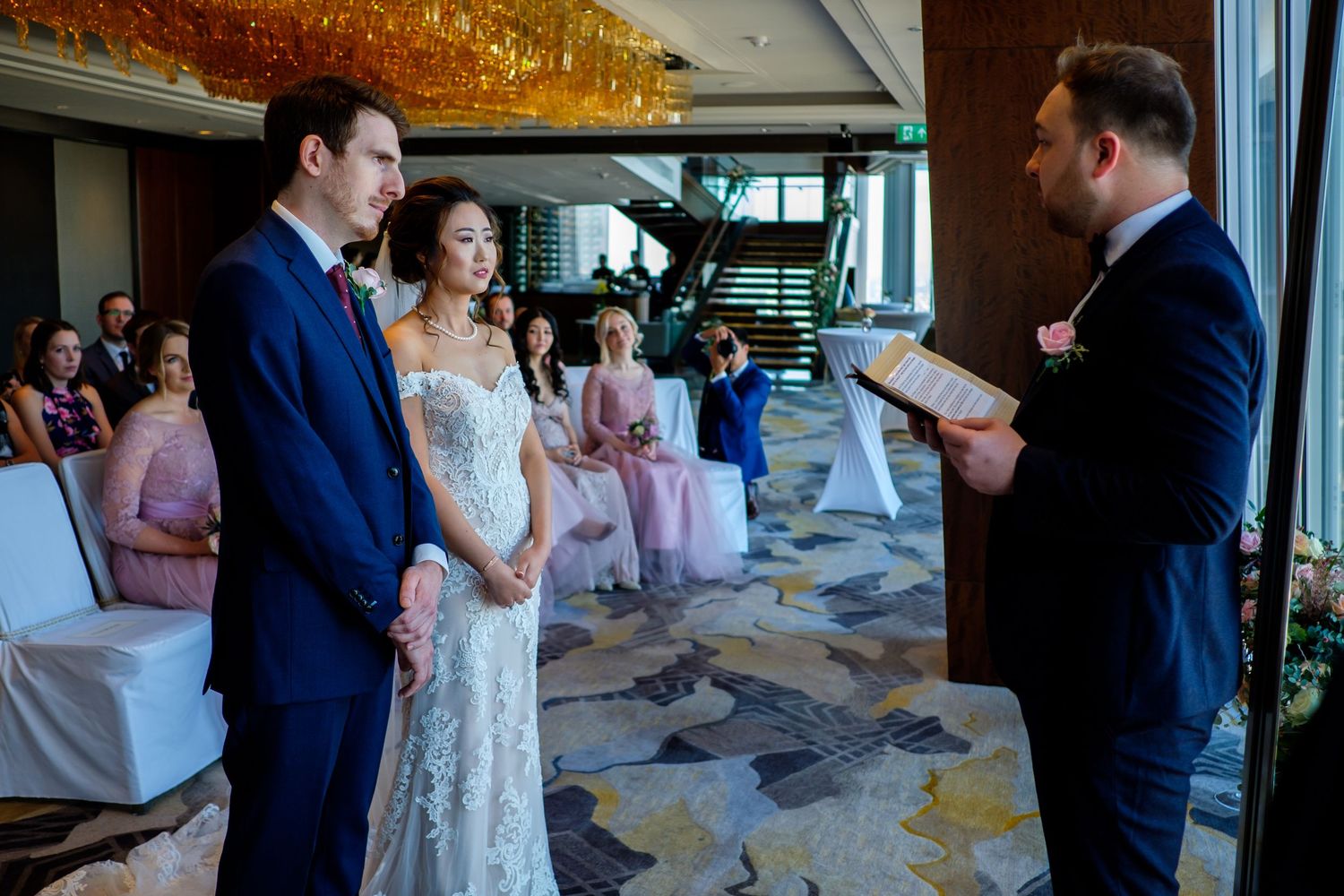 A wedding ceremony moment with guests in formal attire gathered in an elegant indoor venue.