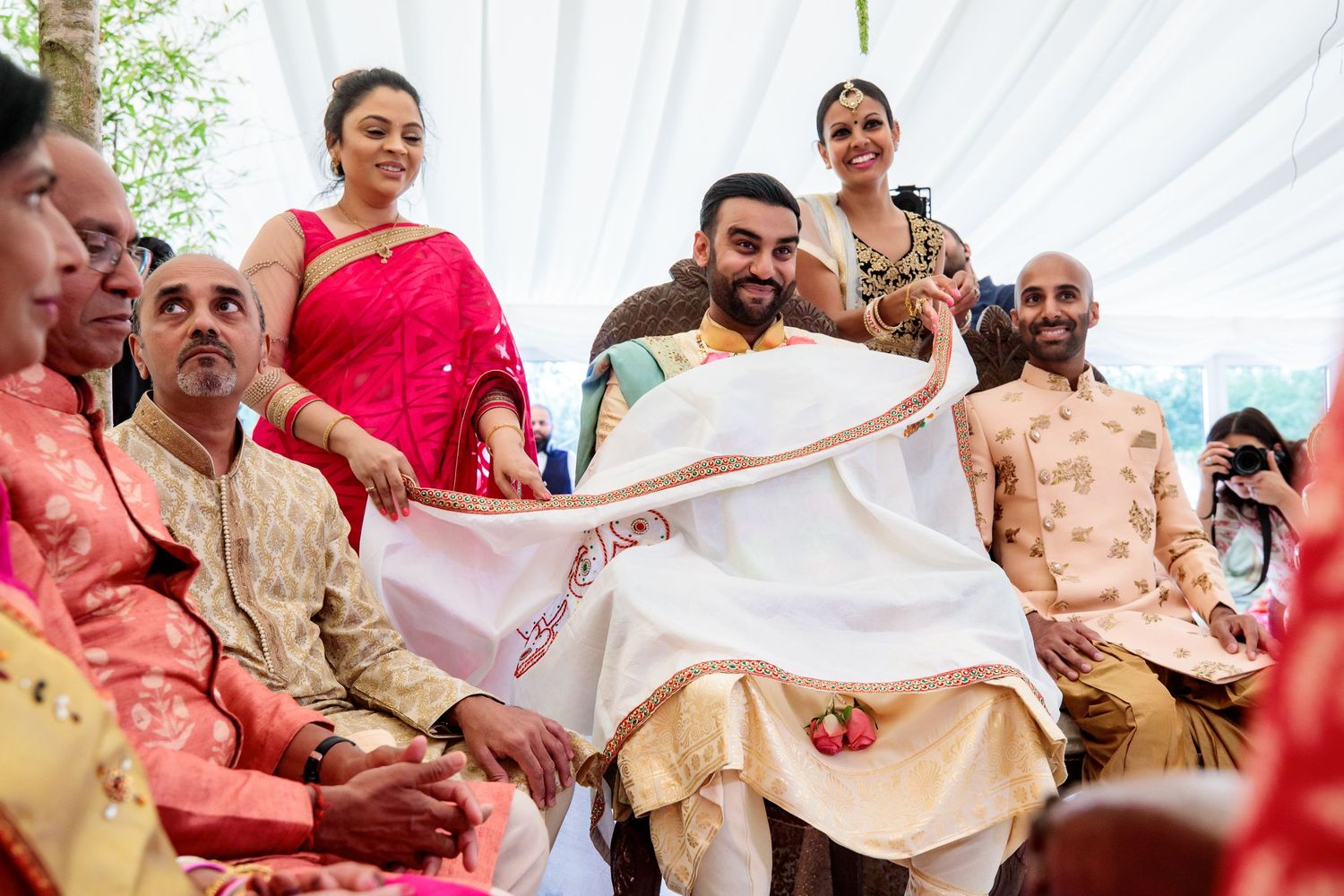 Traditional Indian wedding ceremony guests gather around a white fabric canopy during a cultural celebration.