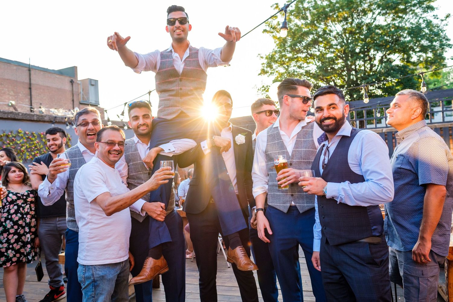 A group of wedding guests dance and celebrate together on an outdoor patio during a festive reception.