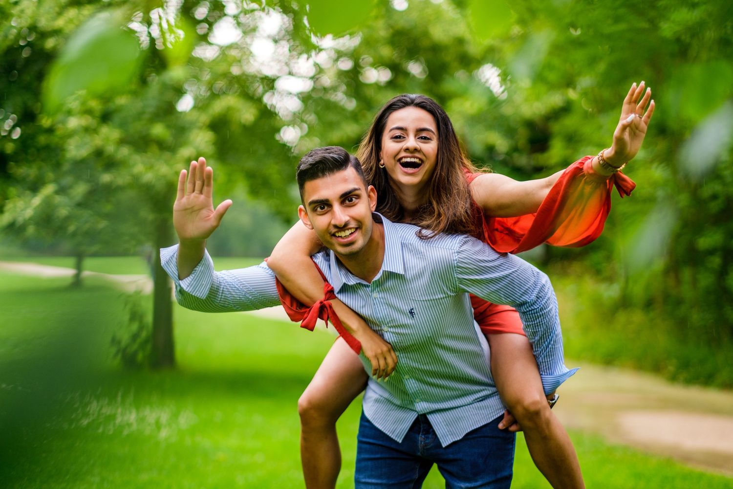 A couple enjoying a playful moment in a lush green park setting during a summer day.