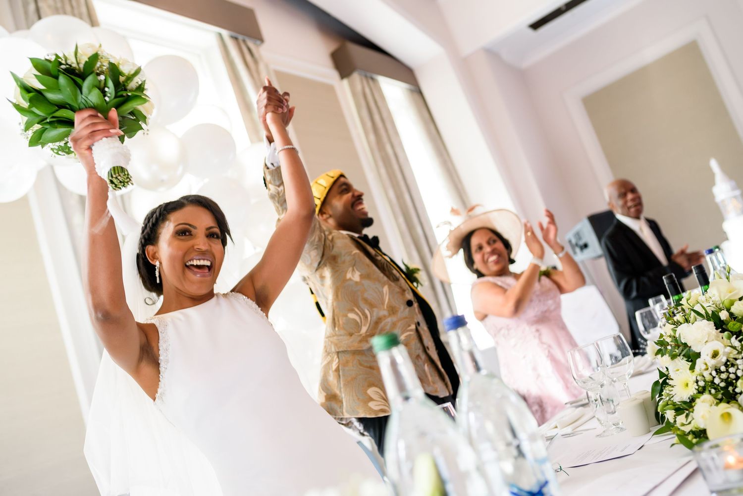 Wedding celebration with guests dancing and laughing in a bright indoor venue with white decor.