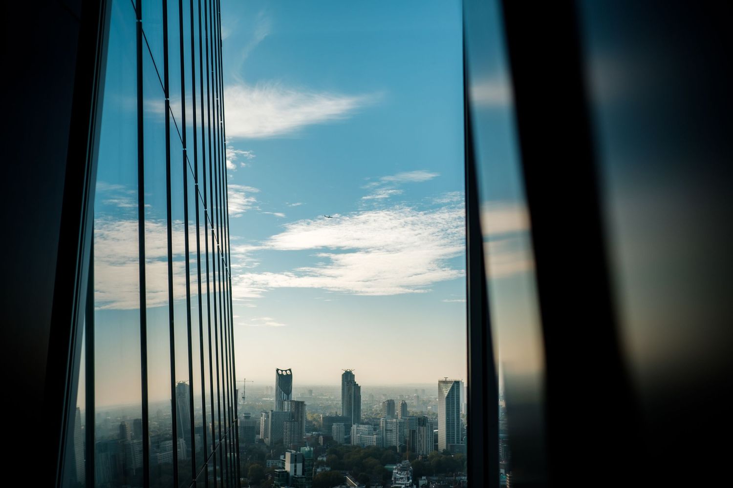 Modern skyscraper buildings reflect dramatic sunset sky with silhouetted architecture in an urban cityscape.