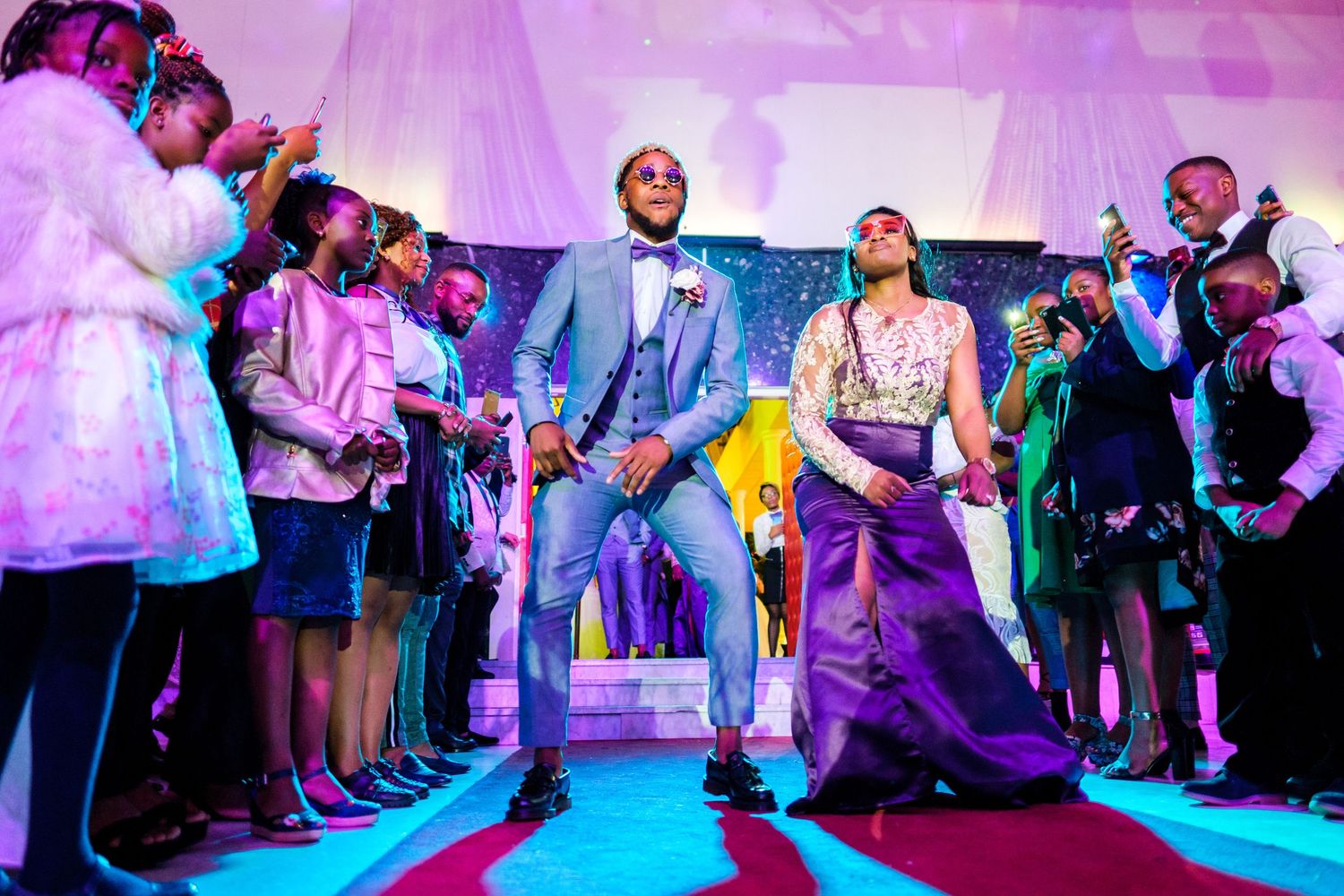Wedding reception dance floor illuminated with purple lighting as guests celebrate.
