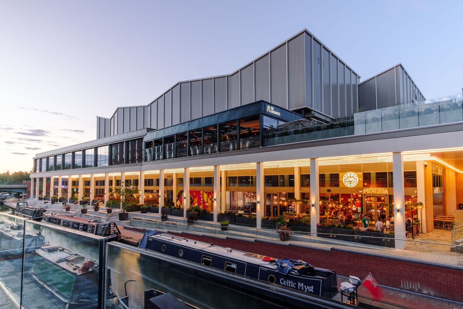 Exterior view of a commercial building with modern architectural design and illuminated storefronts at dusk.